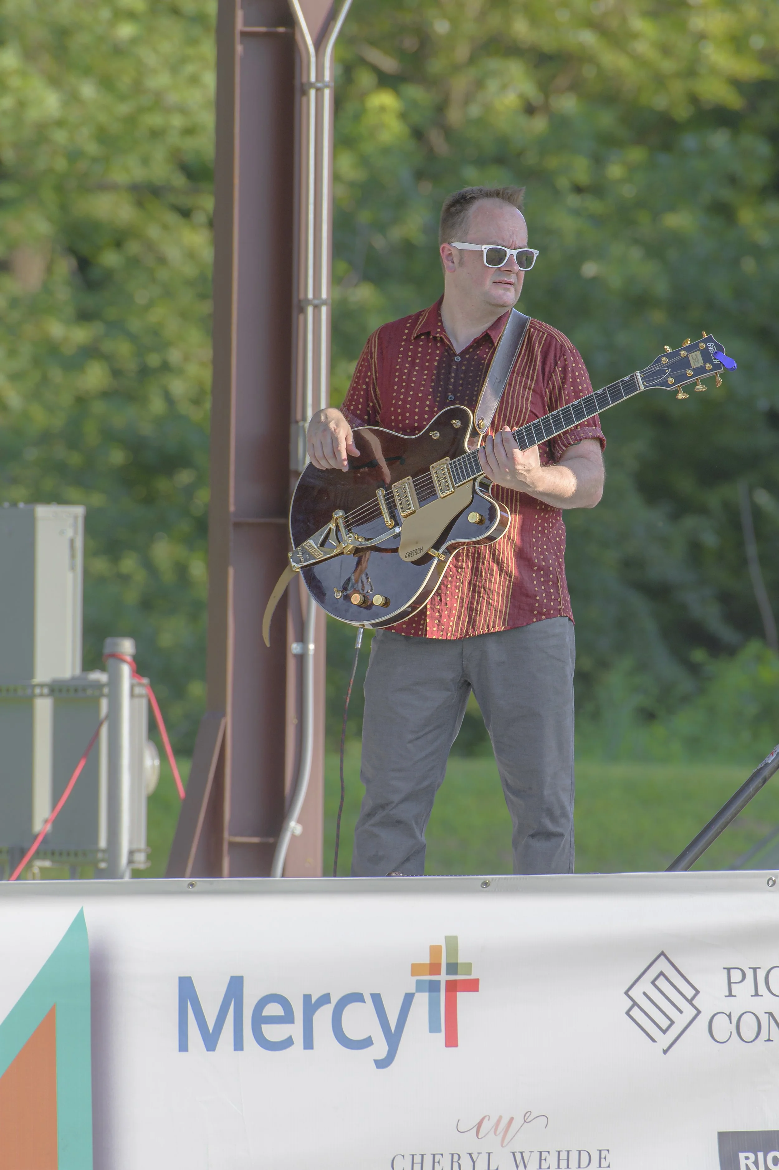 A guitarist in a red shirt and white sunglasses holds a hollow-body electric guitar at the 2022 ECGA Concert.