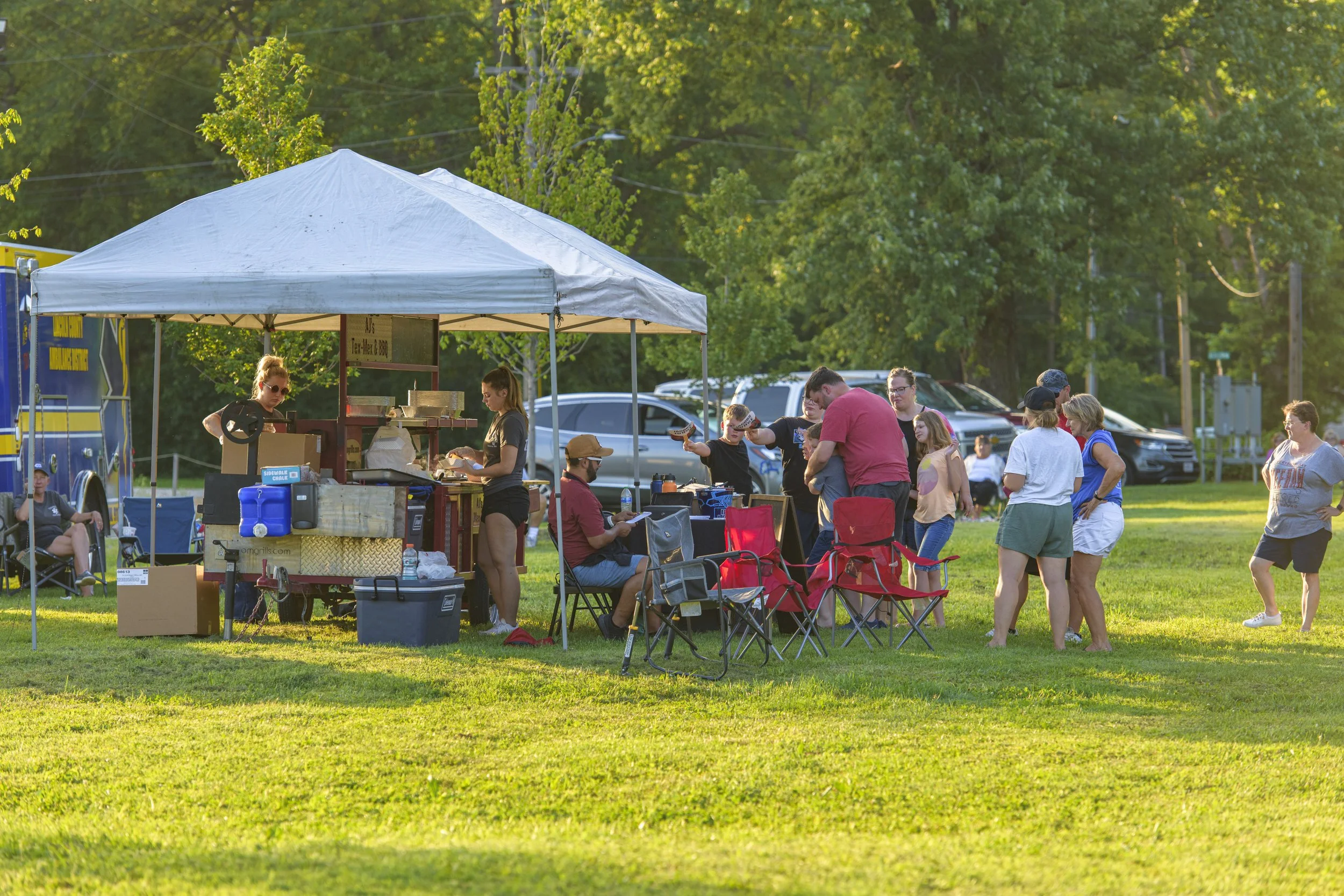 Concertgoers gather around a canopy and folding chairs on the grass at the 2022 ECGA Concert.