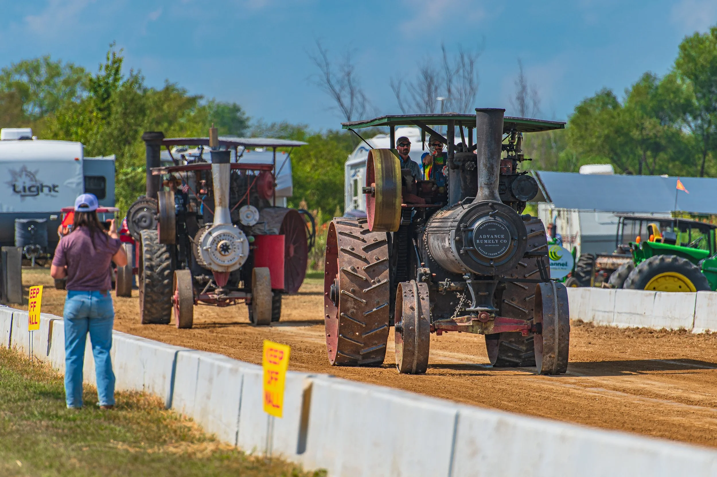 Two steam traction engines travel along the track as an onlooker watches from behind the barrier at the 2022 Old Thresher Days.