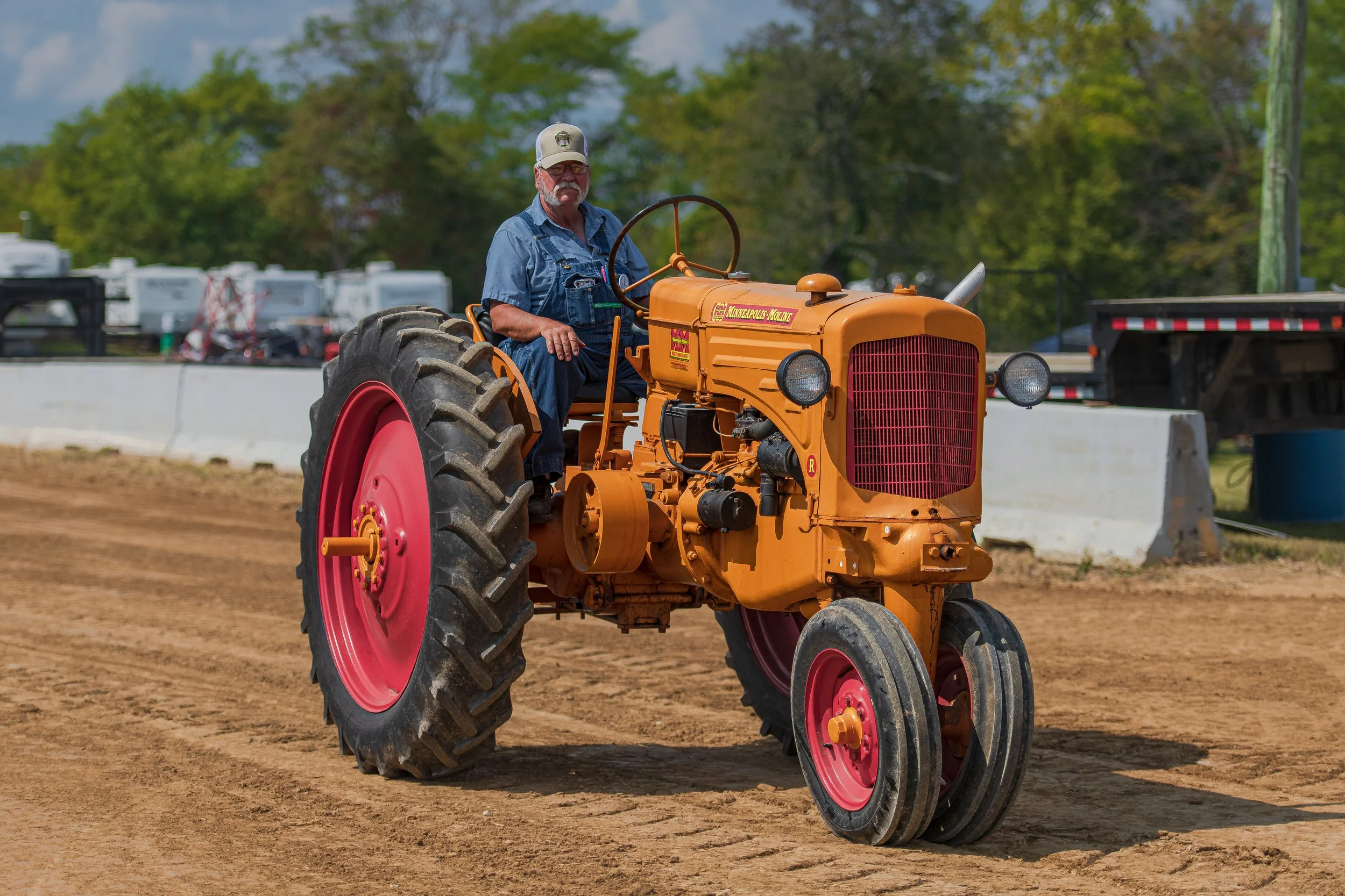 A driver steers an orange vintage tractor with red wheels along the dirt track at the 2022 Old Thresher Days.