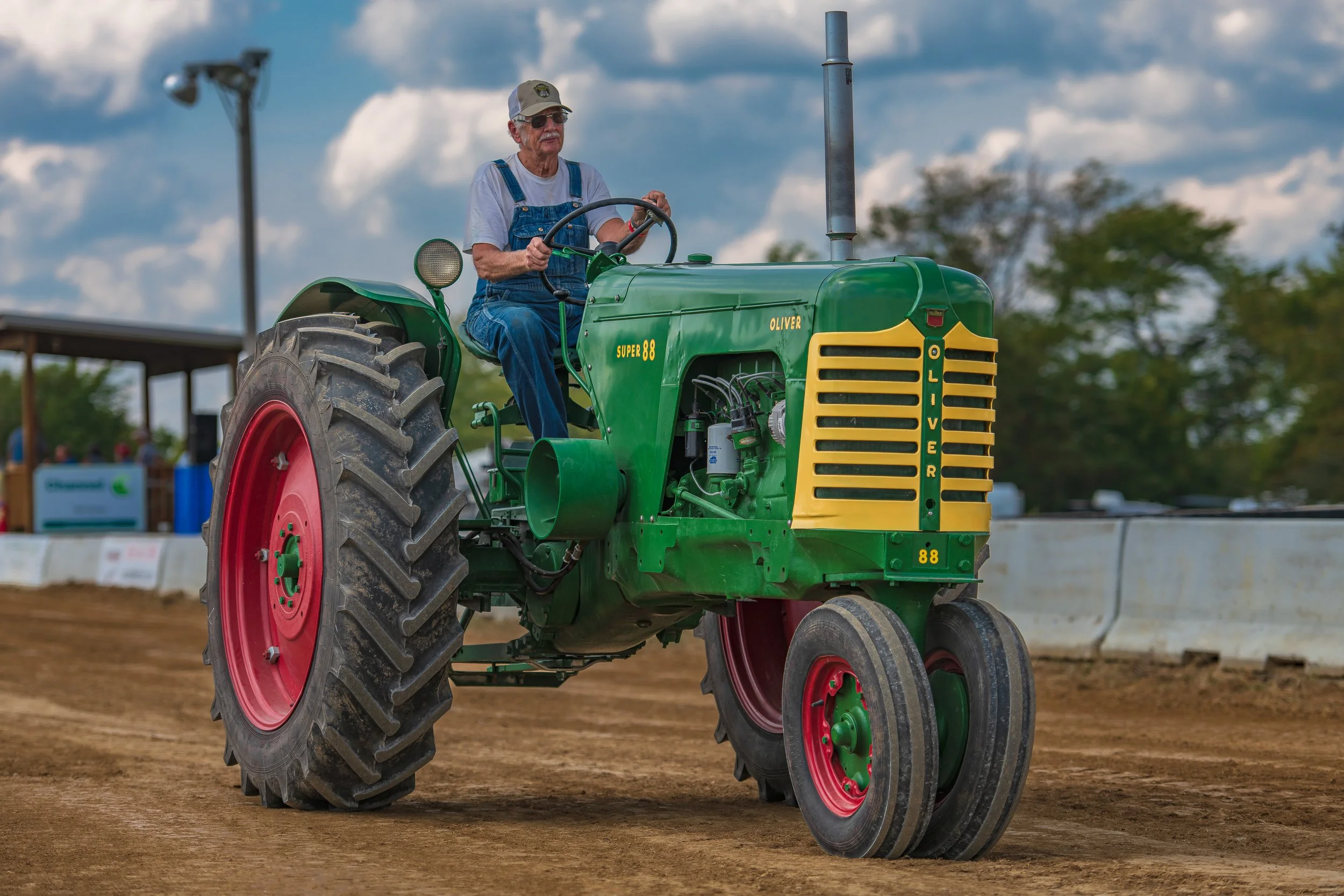 A driver in overalls steers a green tractor with red wheels at the 2022 Old Thresher Days.