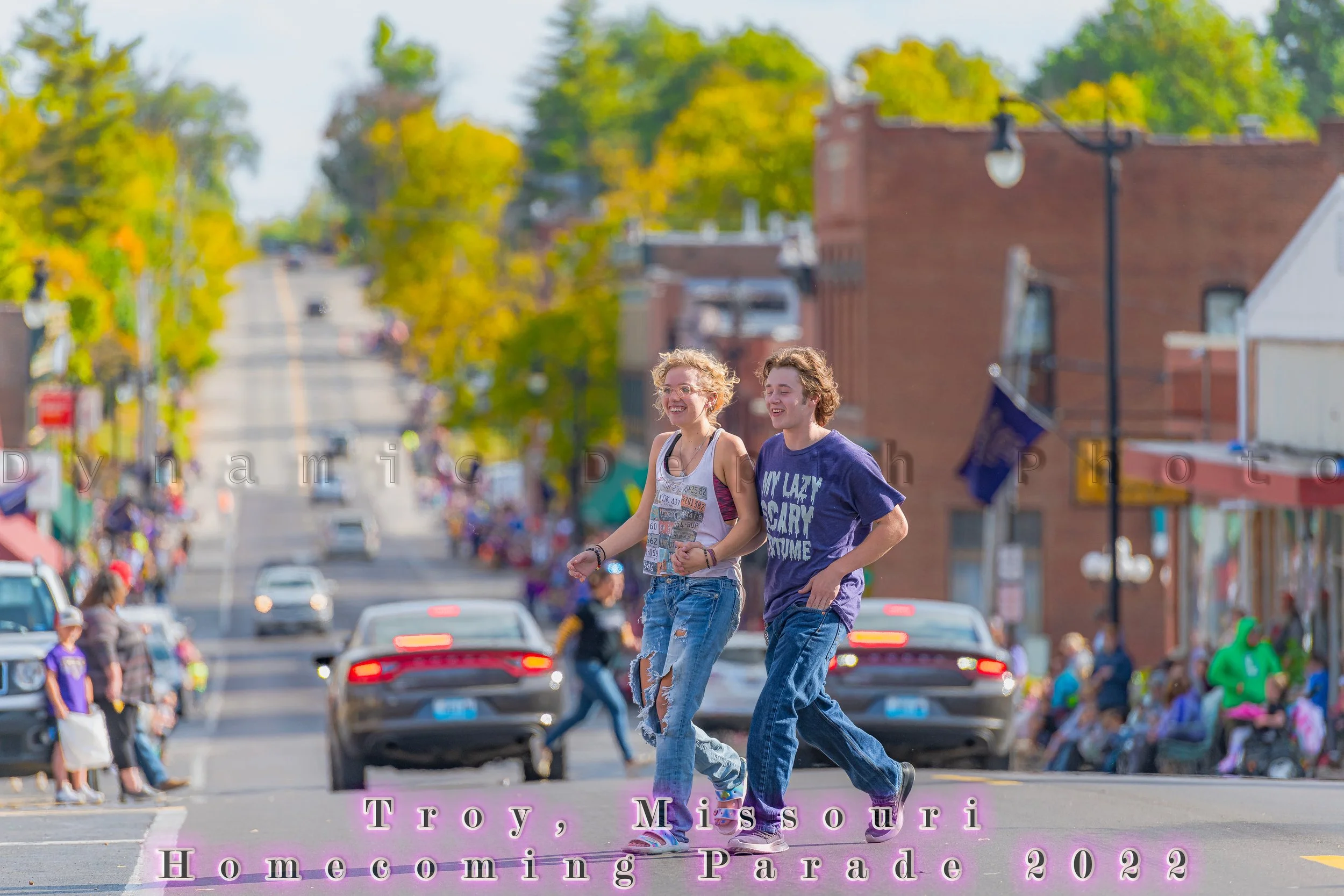 Two participants walk ahead of vehicles on the spectator-lined street during the 2022 Troy Homecoming Parade.