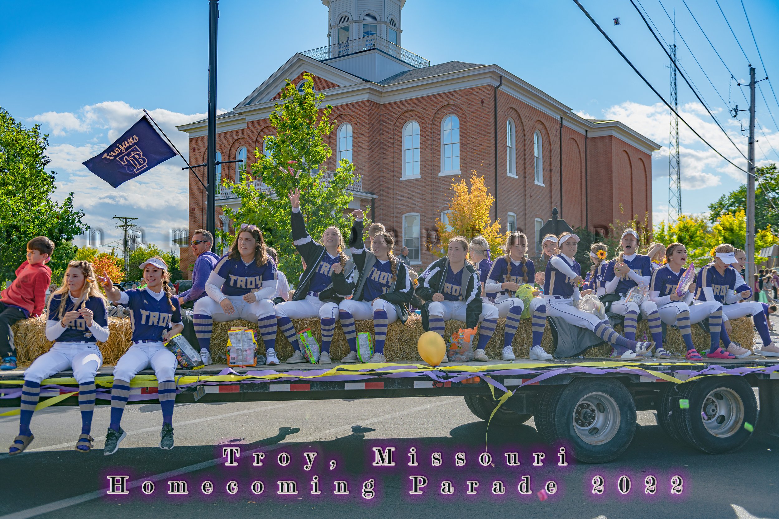 Team members in navy-and-white uniforms ride on a flatbed float during the 2022 Troy Homecoming Parade.