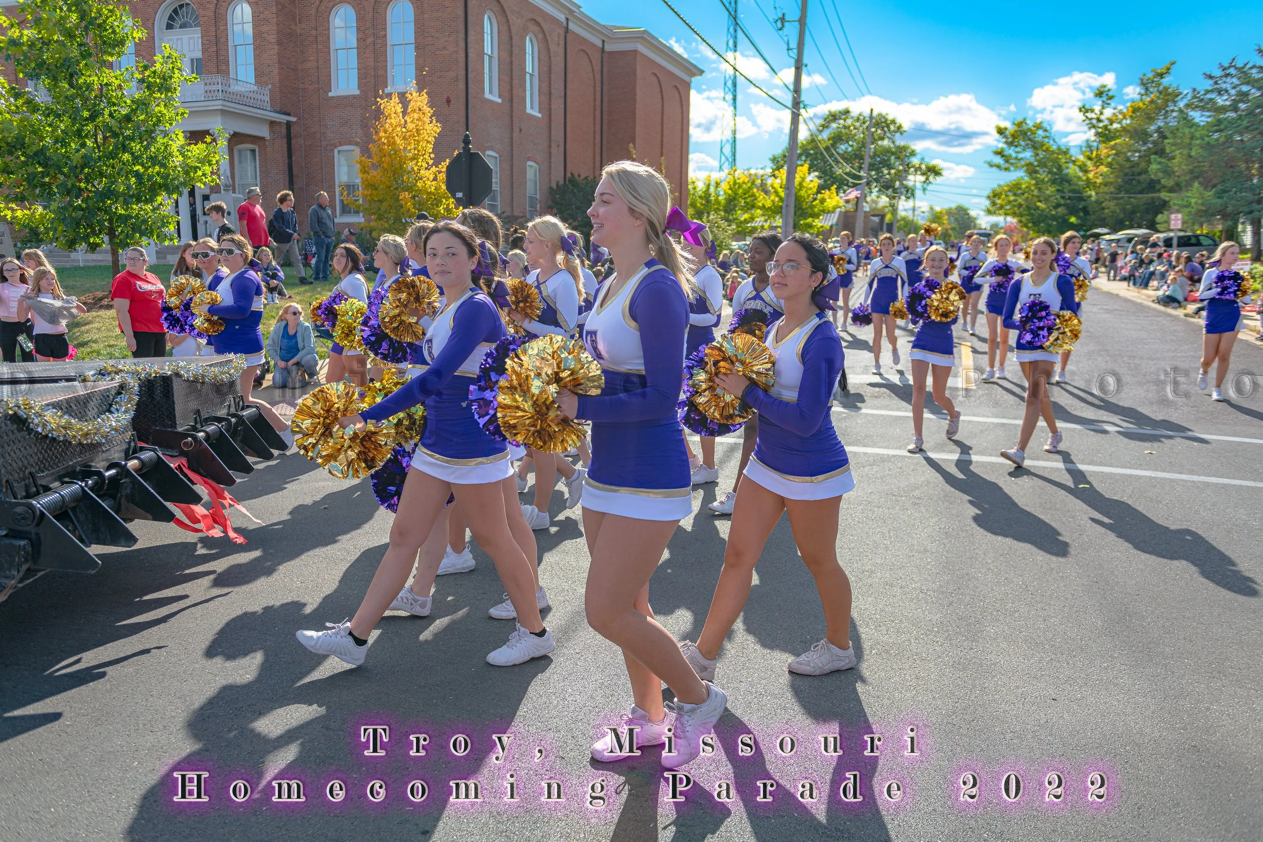 Cheerleaders carry gold and purple pom-poms past the spectators during the 2022 Troy Homecoming Parade.