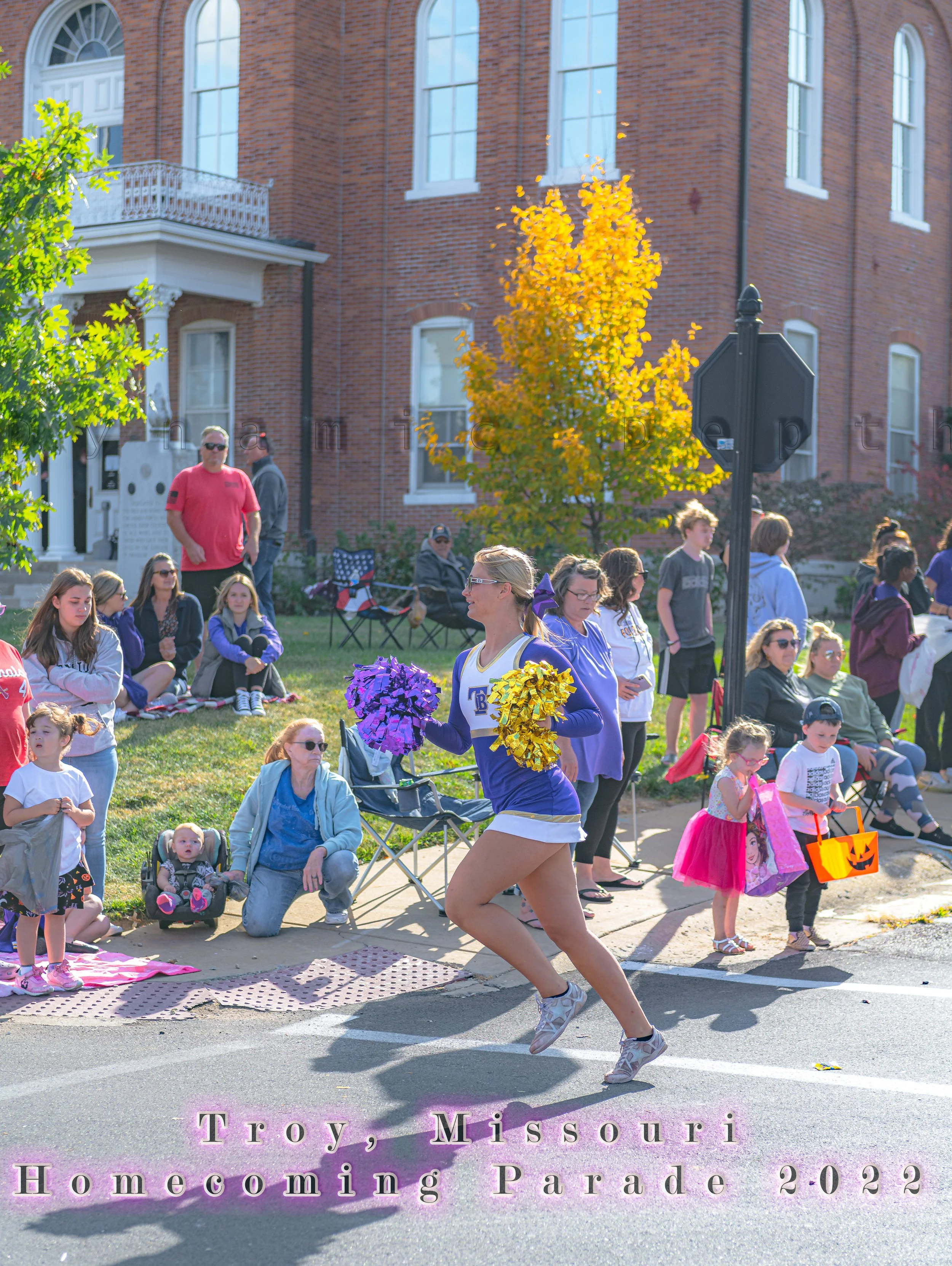 A cheerleader carries pom-poms past seated spectators during the 2022 Troy Homecoming Parade.