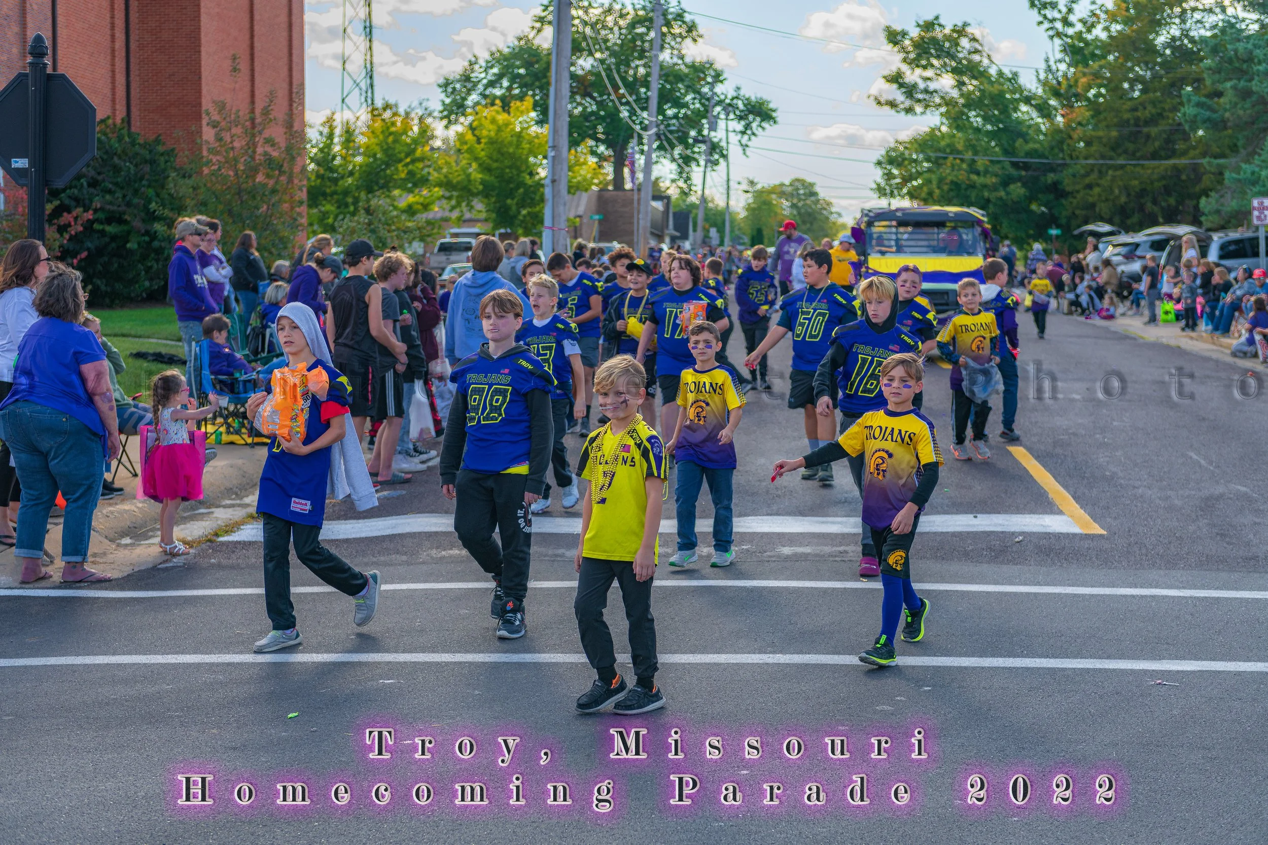 Young participants in football jerseys walk along the route carrying bags and buckets during the 2022 Troy Homecoming Parade.