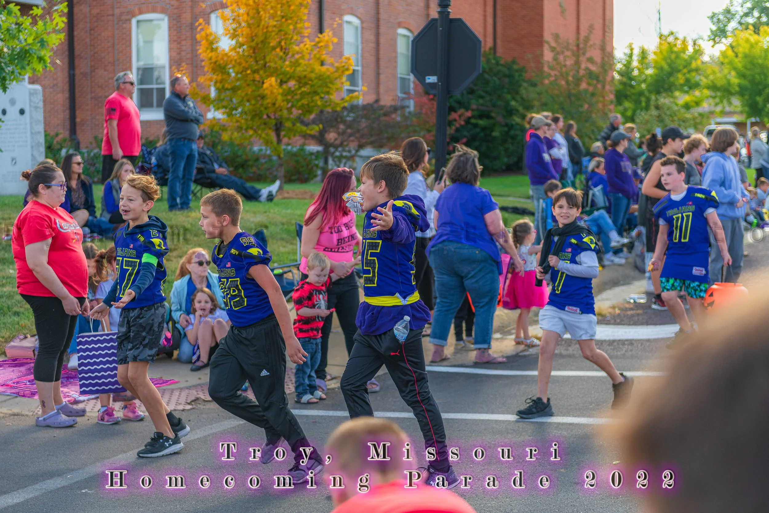 Jersey-clad participants pass spectators seated beside the street during the 2022 Troy Homecoming Parade.