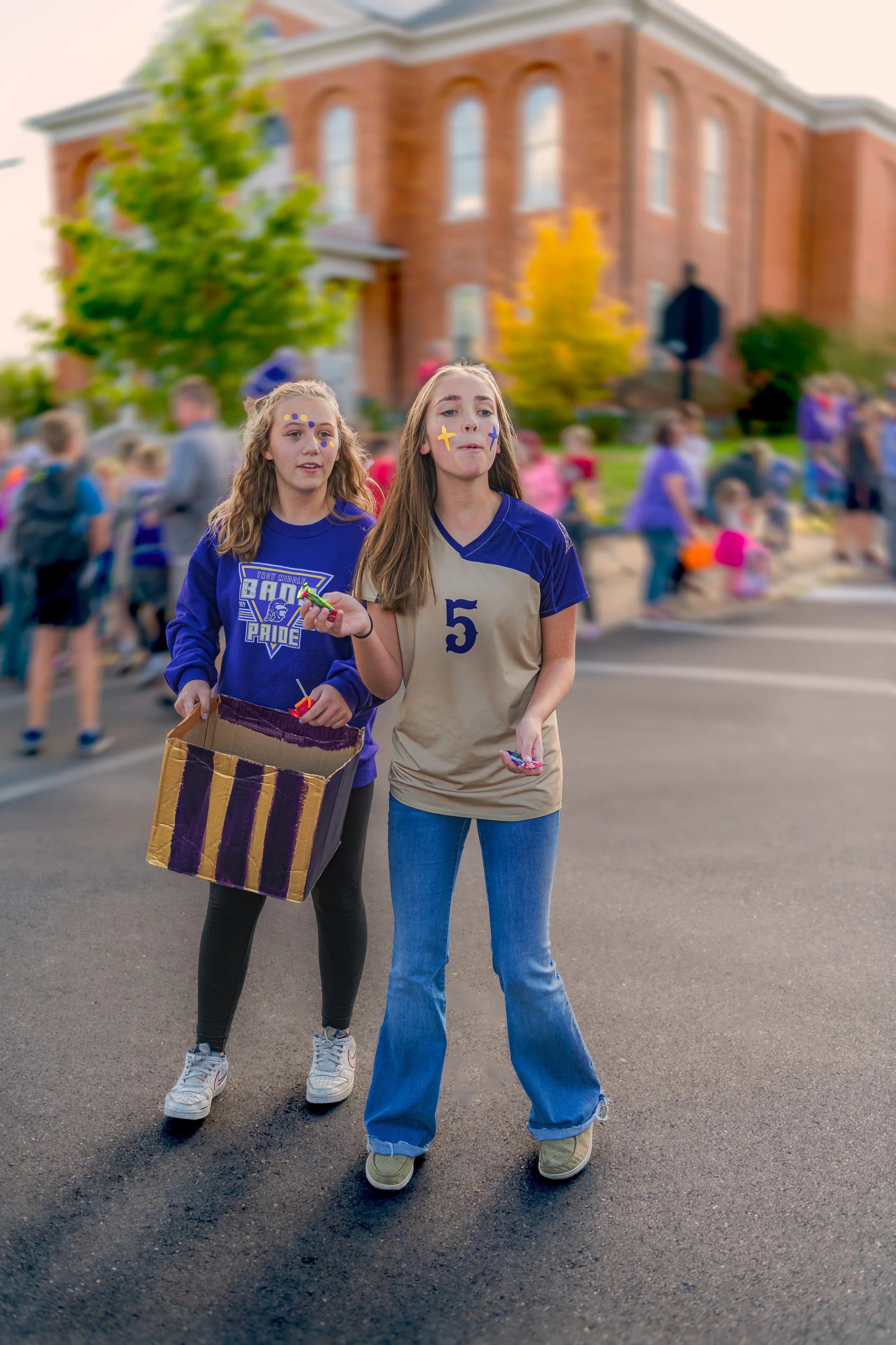 Two participants walk together, one carrying a purple-and-gold box during the 2022 Troy Homecoming Parade.