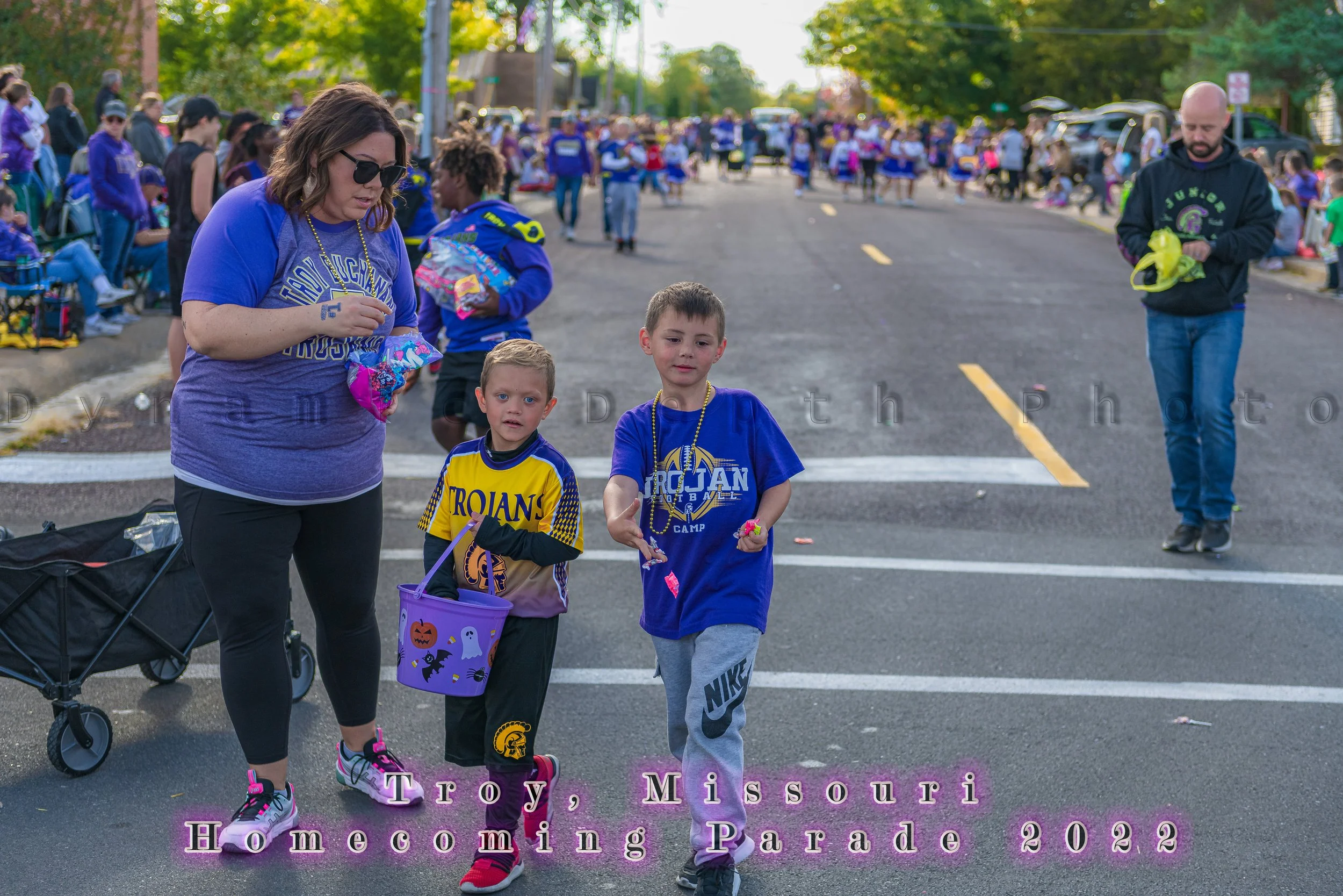 An adult walks beside two children carrying containers along the route during the 2022 Troy Homecoming Parade.
