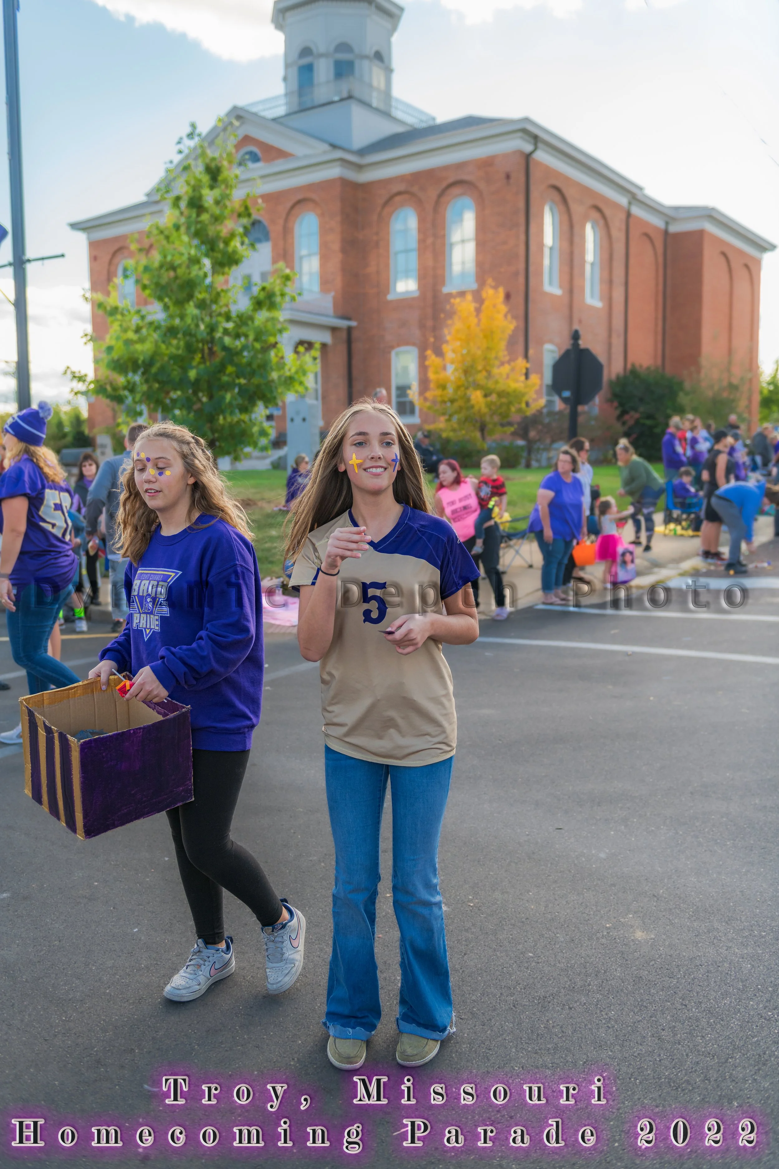 Two participants pass the red-brick building carrying a decorated box during the 2022 Troy Homecoming Parade.