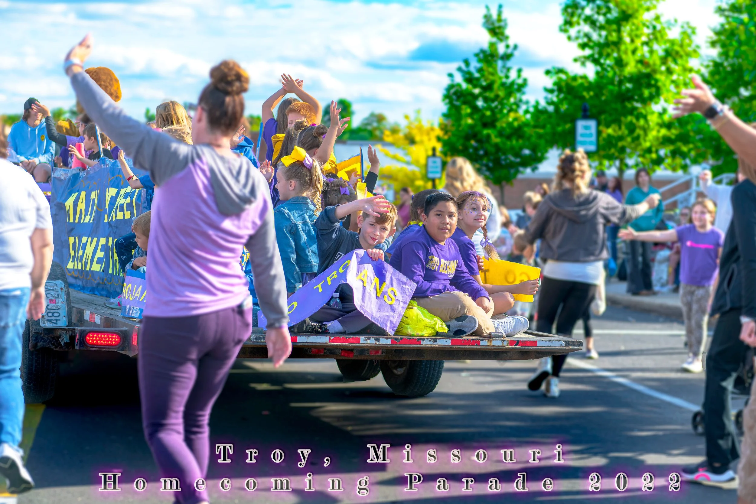 Riders wave from a decorated trailer as accompanying walkers raise their arms during the 2022 Troy Homecoming Parade.