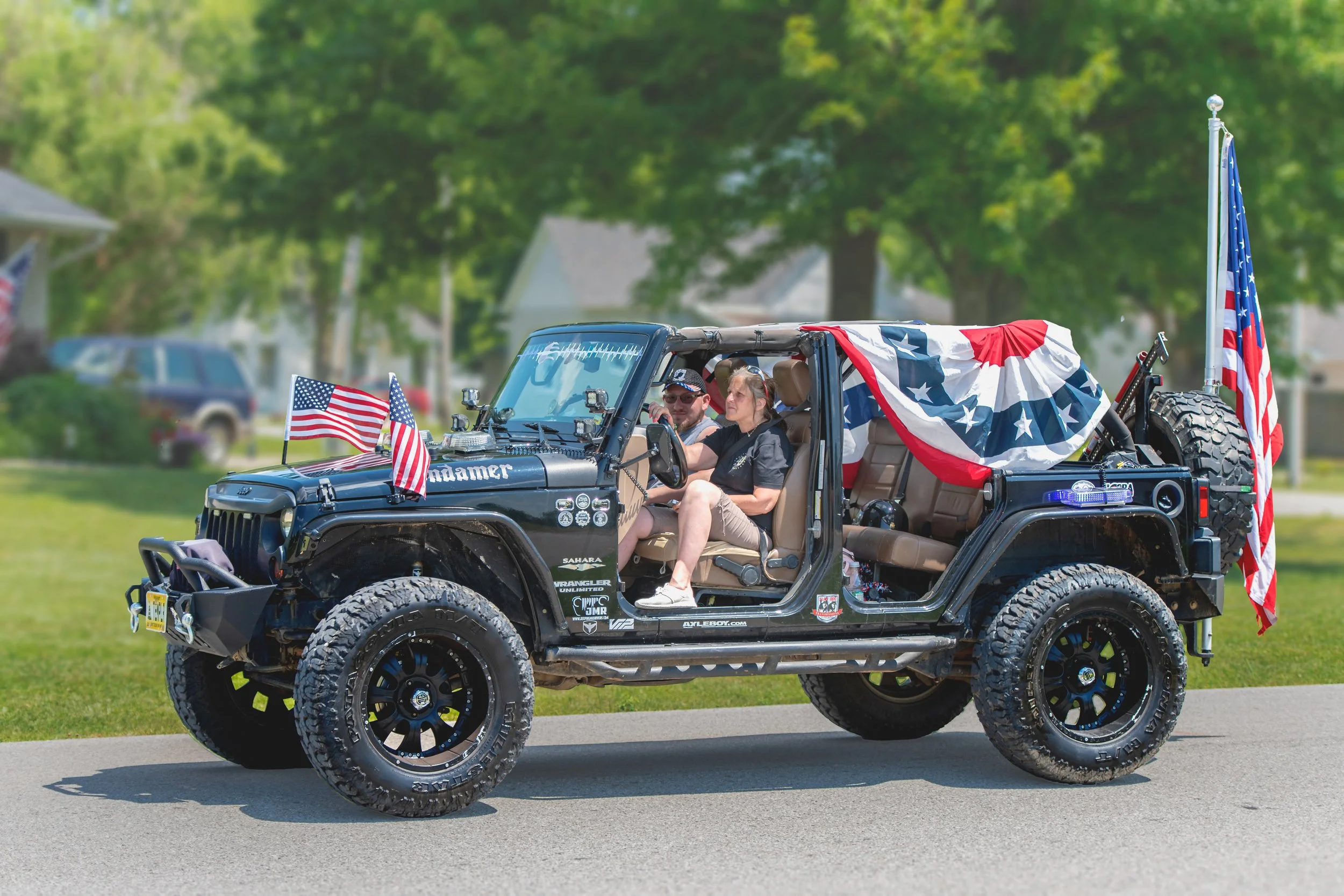A dark open-sided Jeep carries American flags and red, white, and blue bunting during the 2022 July 4th Hawk Point Parade.