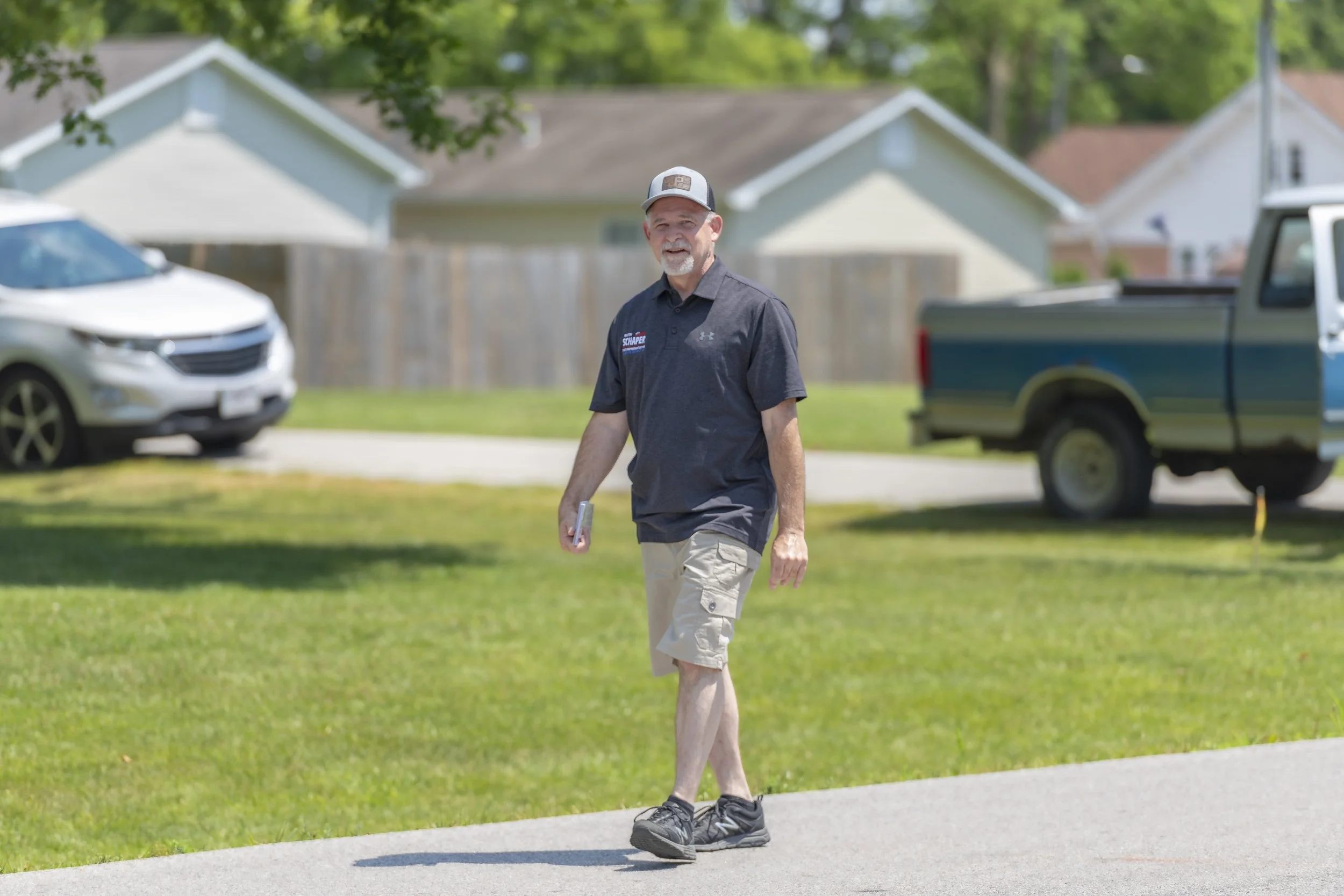 A participant in a dark polo shirt walks along the parade route during the 2022 July 4th Hawk Point Parade.