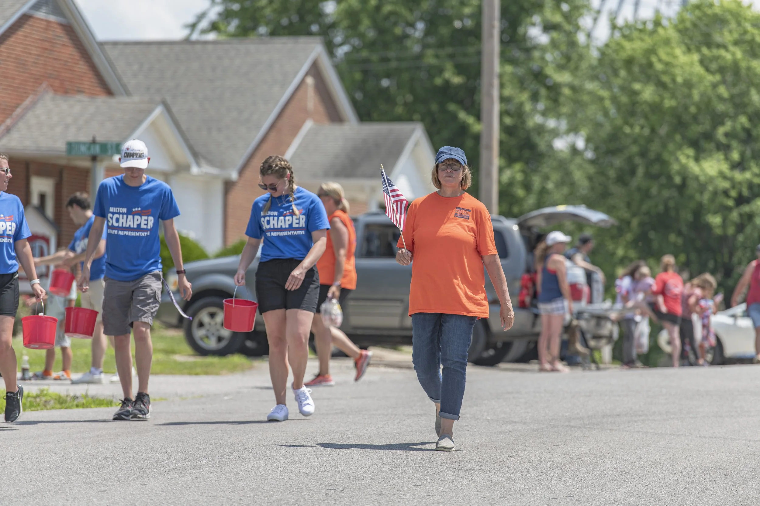 Marchers carry small buckets and an American flag past roadside spectators during the 2022 July 4th Hawk Point Parade.