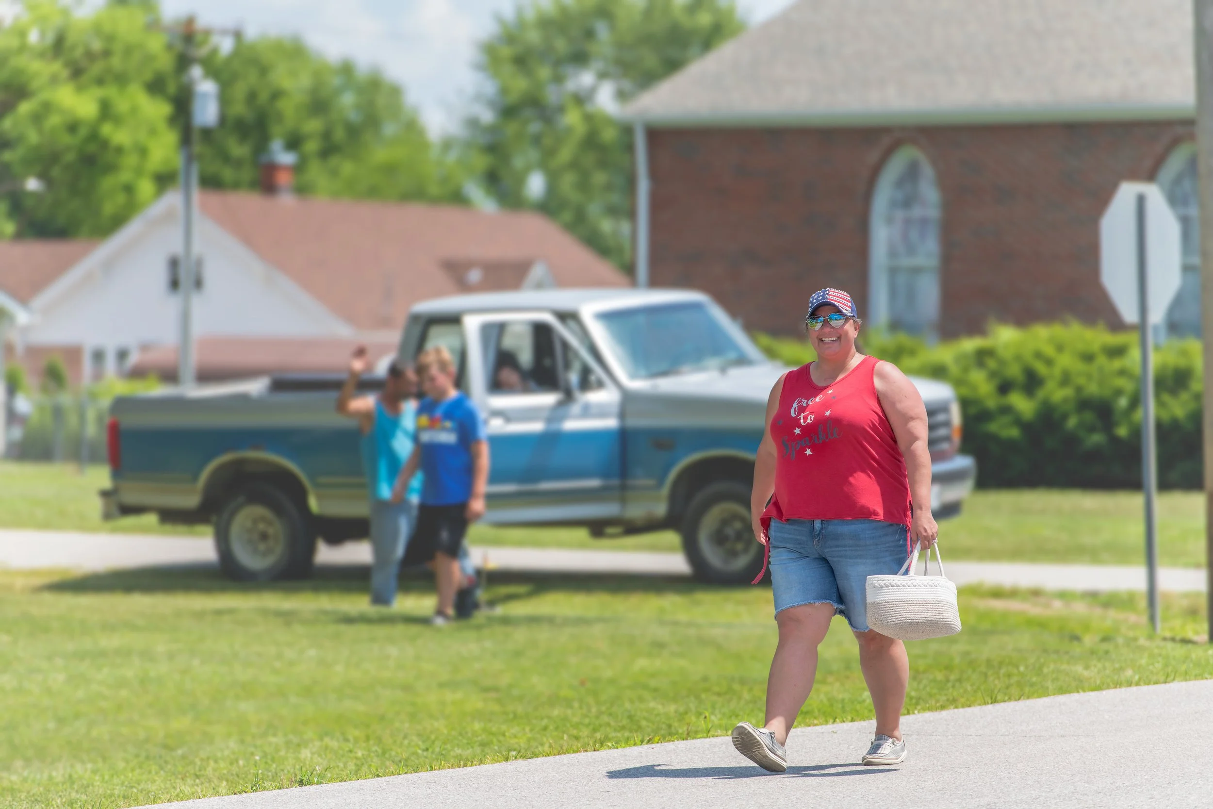A marcher in a red top carries a white bucket along the road during the 2022 July 4th Hawk Point Parade.