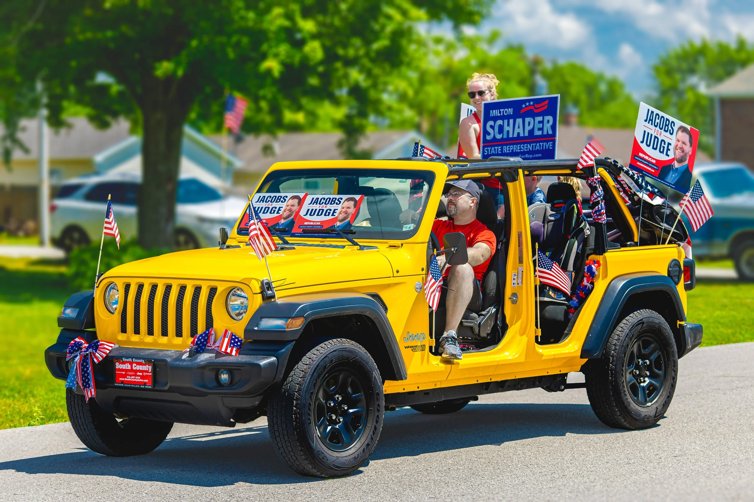 Passengers carry campaign signs in a yellow Jeep decorated with American flags during the 2022 July 4th Hawk Point Parade.