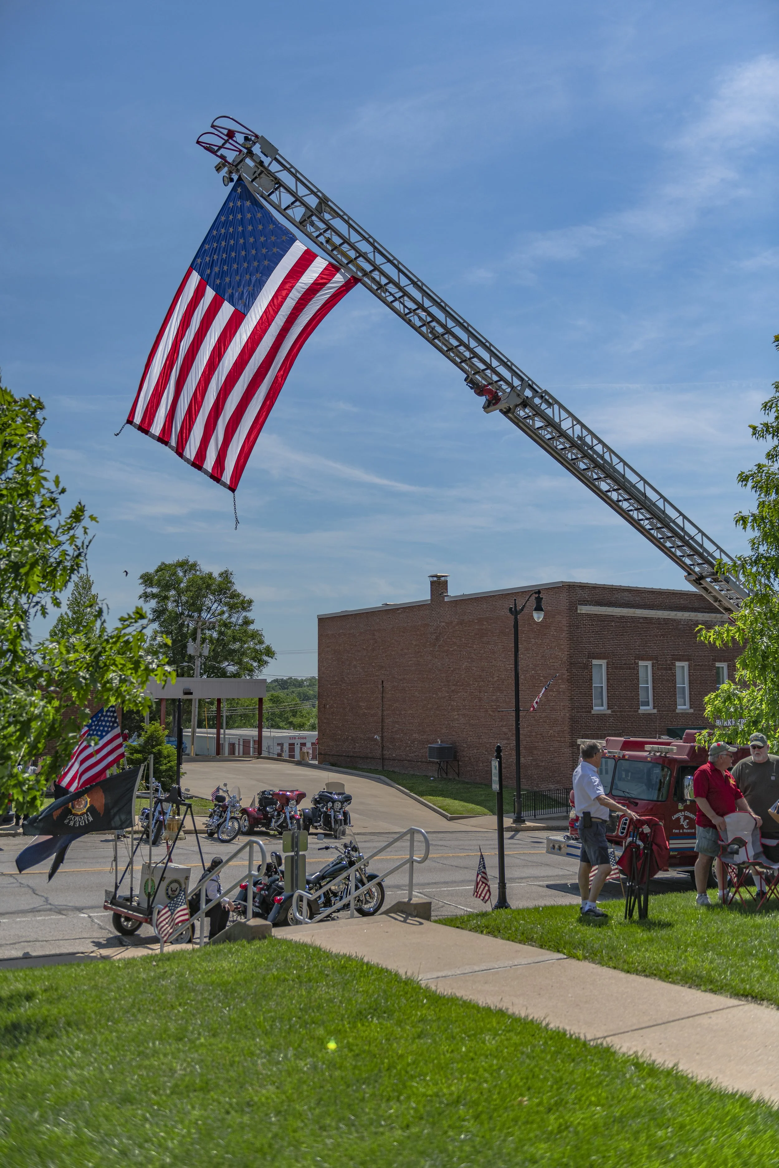 A large American flag hangs from a raised fire-truck ladder above the street at the 2022 Lincoln County Memorial Day service.