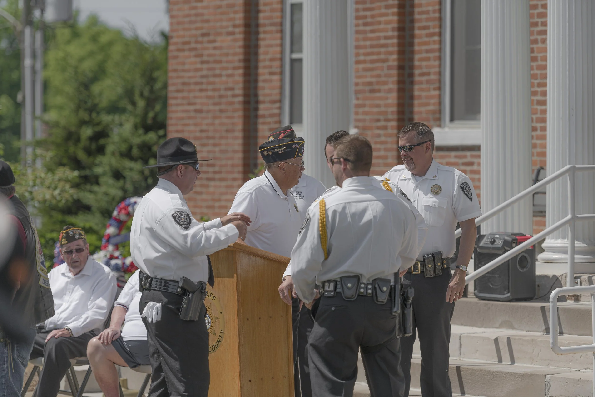 Uniformed participants gather around the lectern beside the building's steps at the 2022 Lincoln County Memorial Day service.