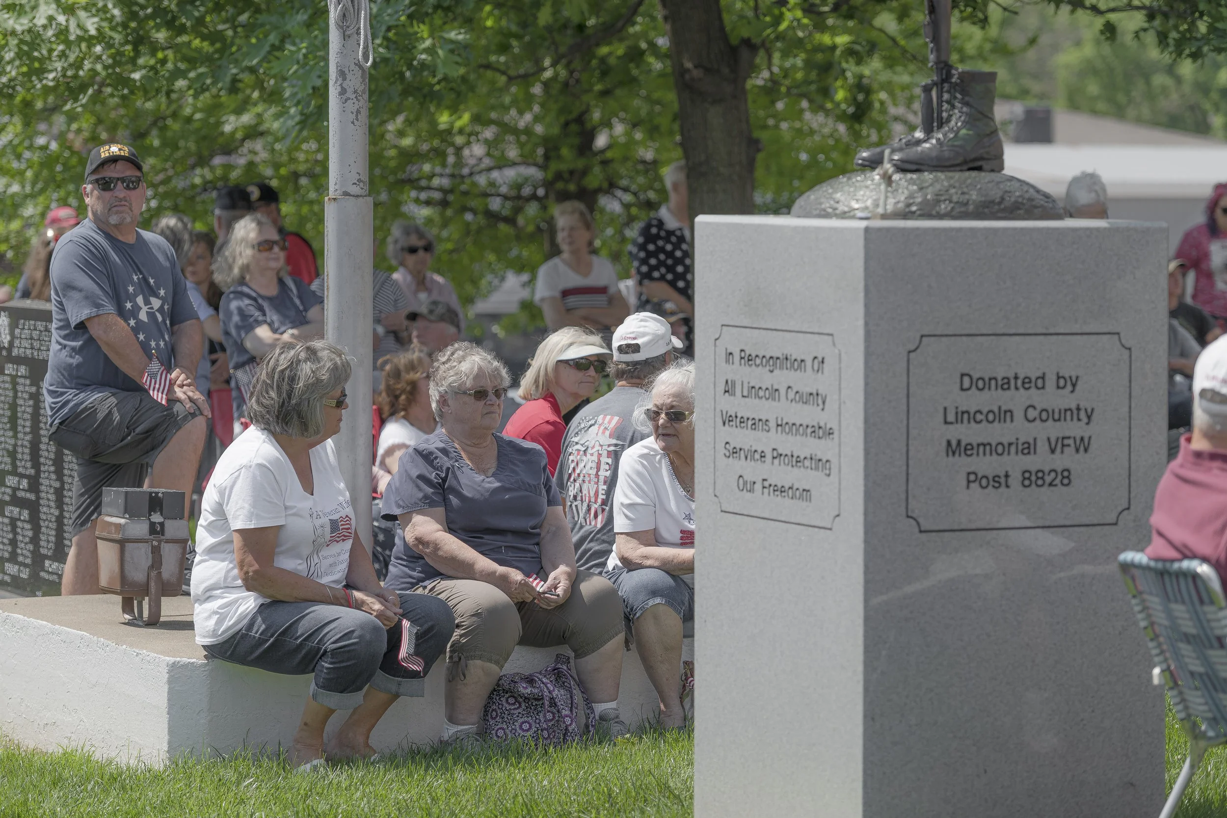 Attendees sit beside a memorial pedestal topped by a sculpture of boots at the 2022 Lincoln County Memorial Day service.
