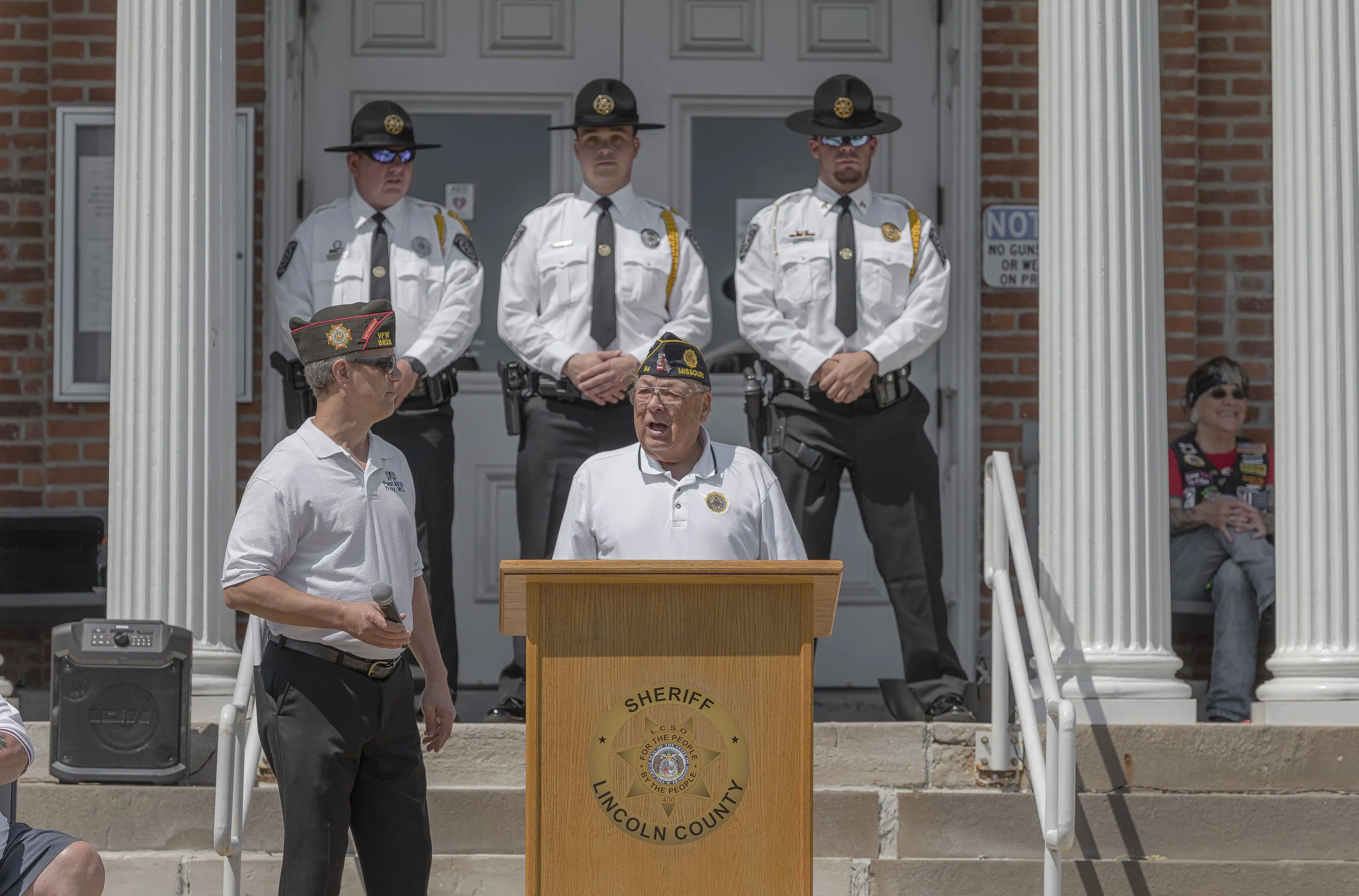 A speaker stands at the lectern with uniformed personnel behind him on the steps at the 2022 Lincoln County Memorial Day service.