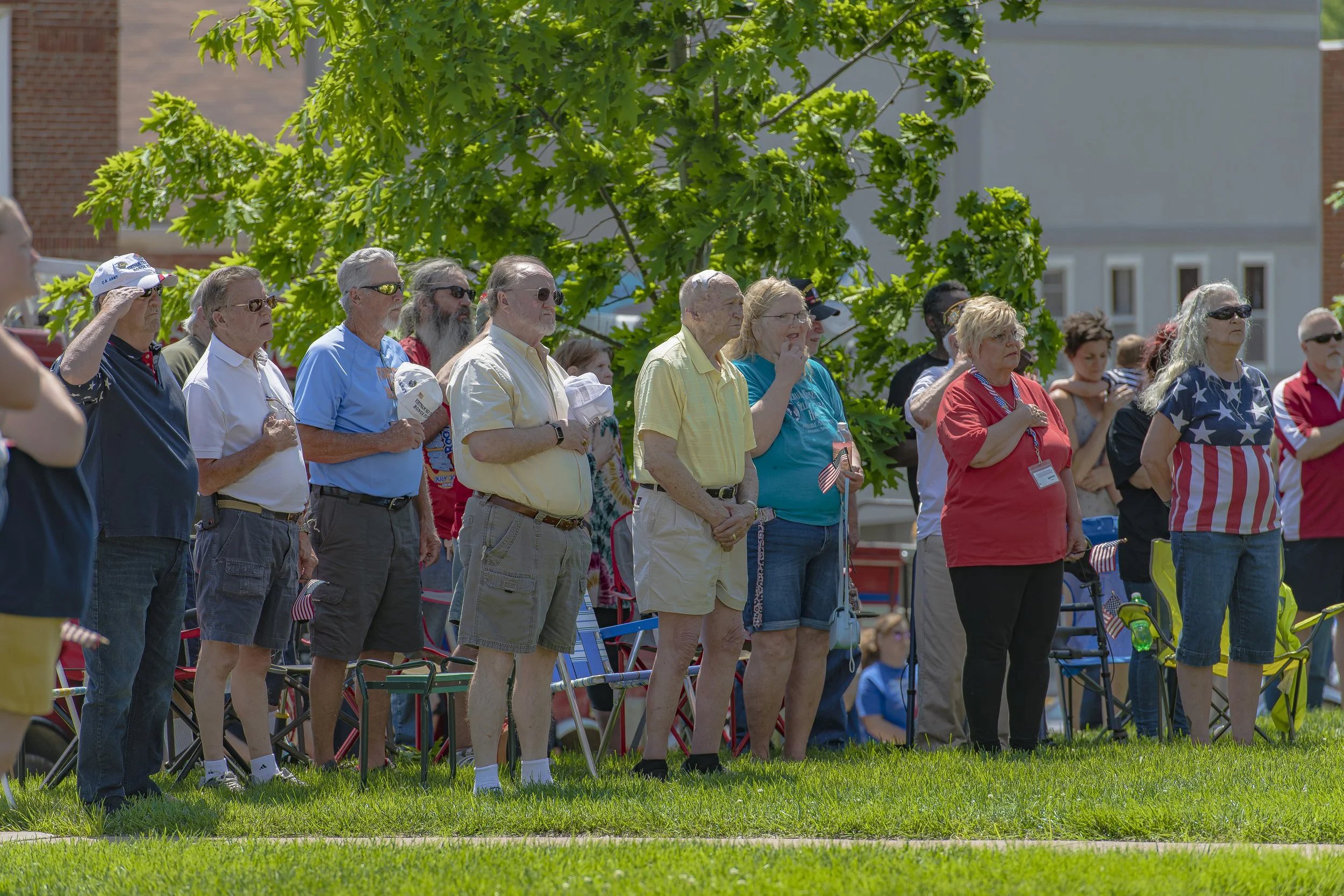 Attendees stand on the lawn, several with hands over their hearts at the 2022 Lincoln County Memorial Day service.