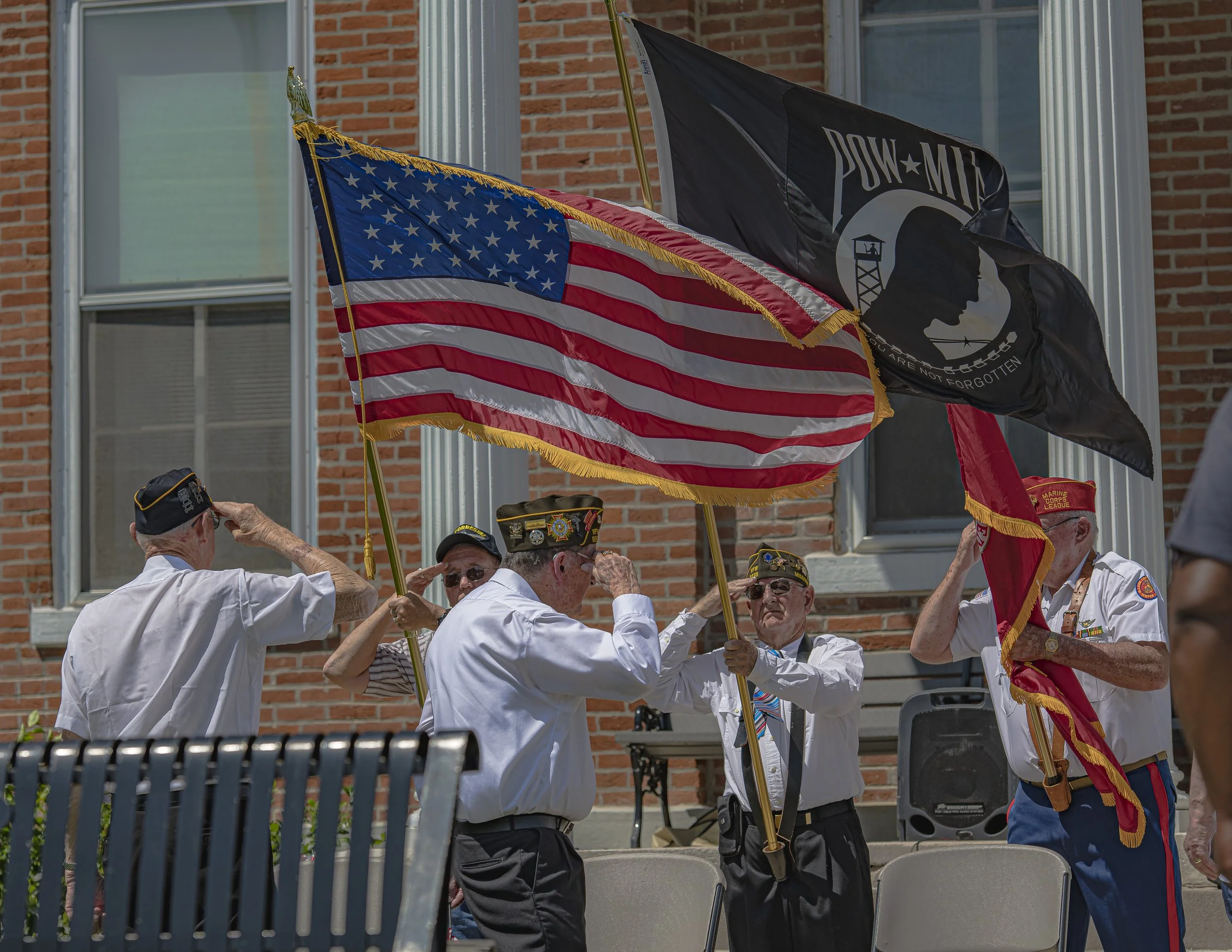 Flag bearers hold American and POW/MIA flags beside a saluting participant at the 2022 Lincoln County Memorial Day service.
