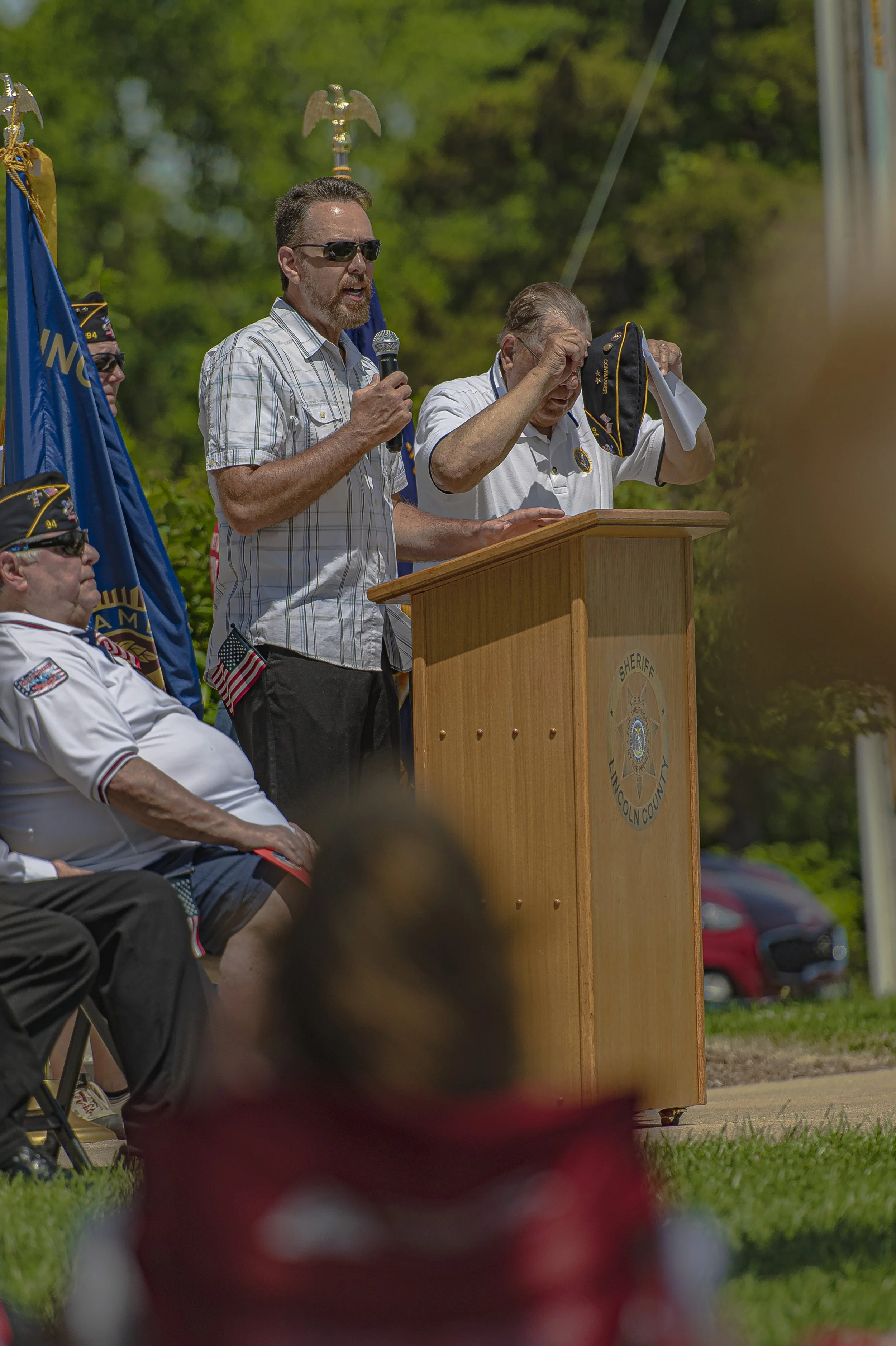 A speaker wearing sunglasses reads from papers at the lectern at the 2022 Lincoln County Memorial Day service.