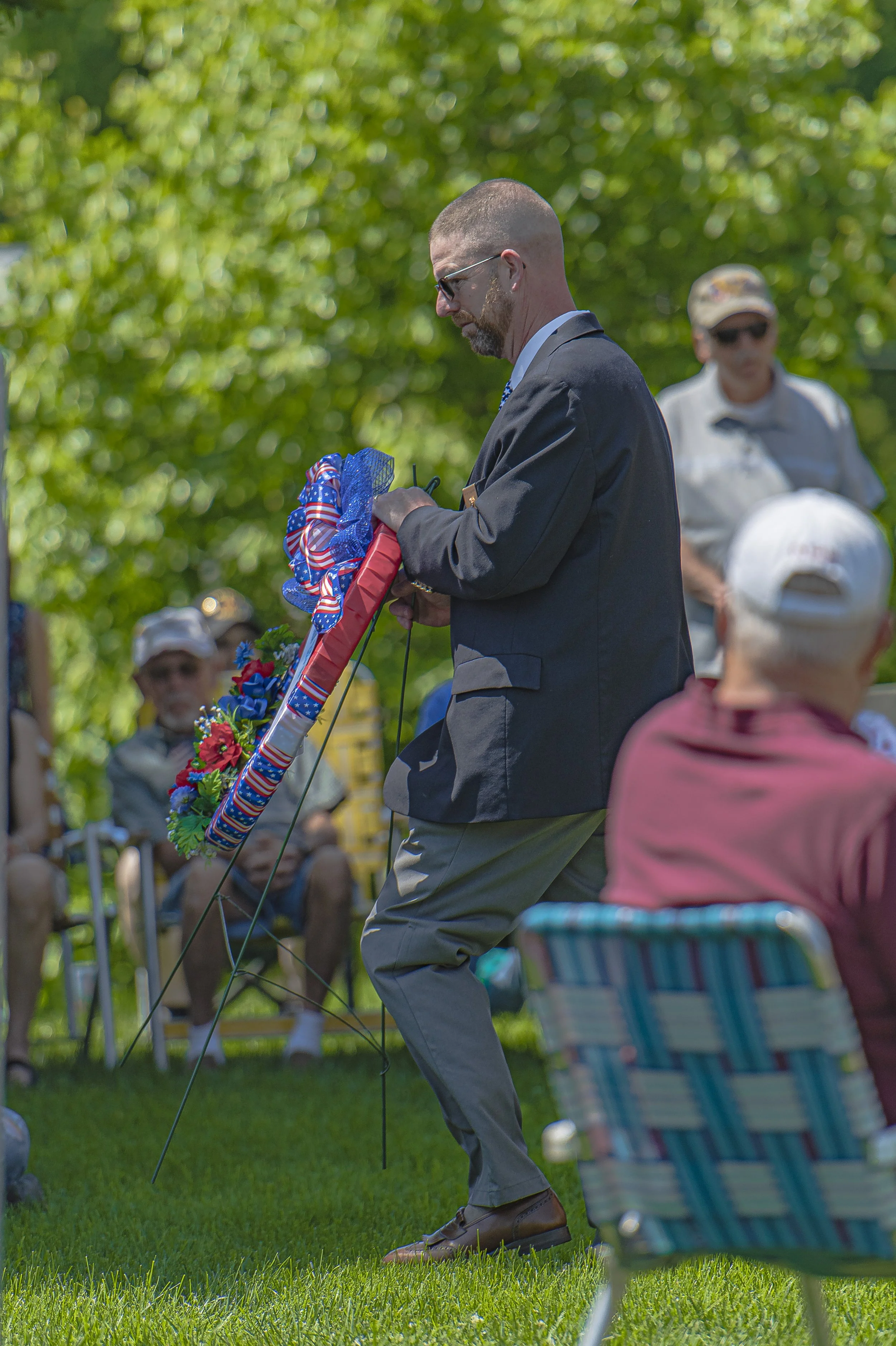 An attendee carries a wreath on a metal stand across the lawn at the 2022 Lincoln County Memorial Day service.