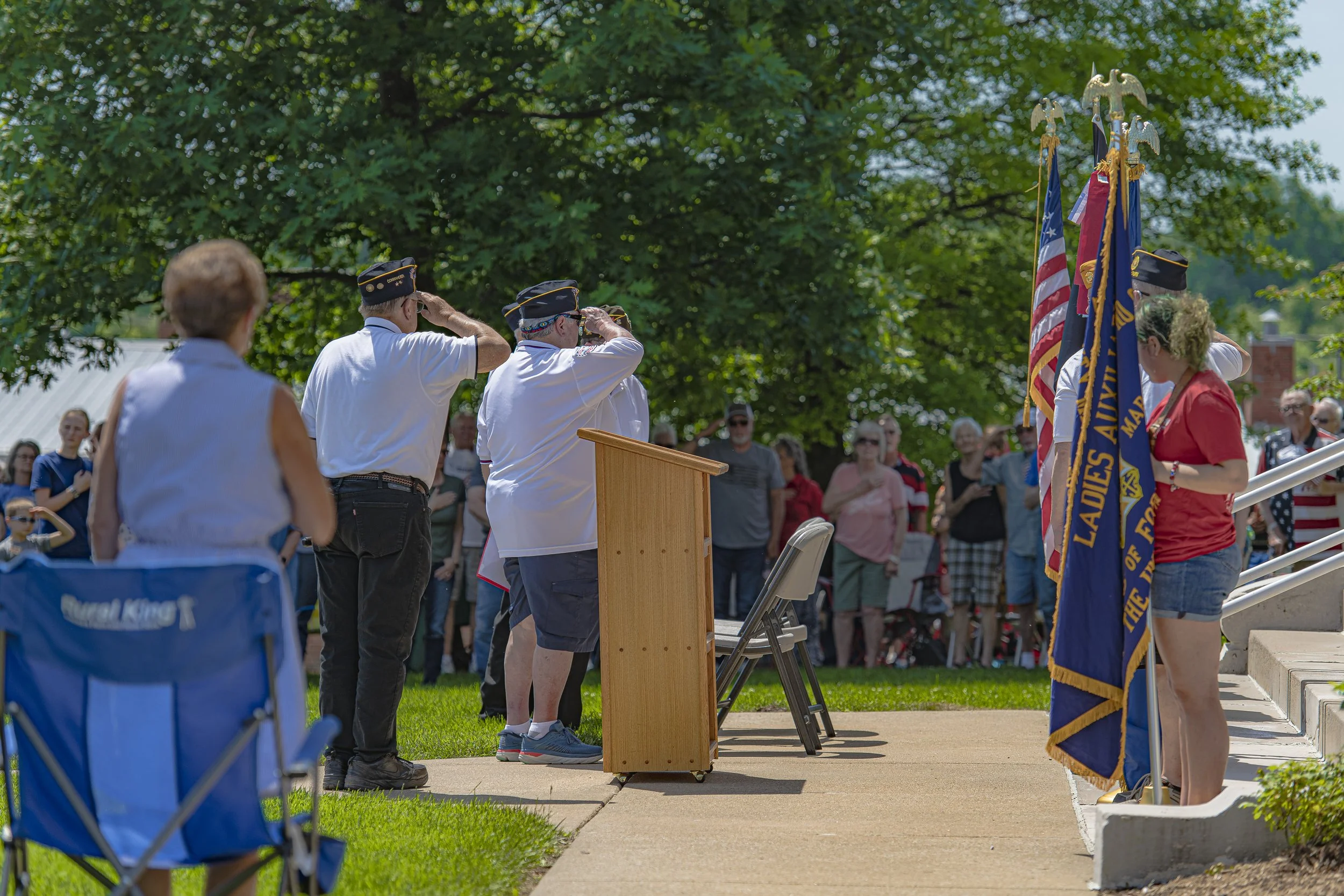 Two participants salute beside the lectern as attendees stand behind them at the 2022 Lincoln County Memorial Day service.