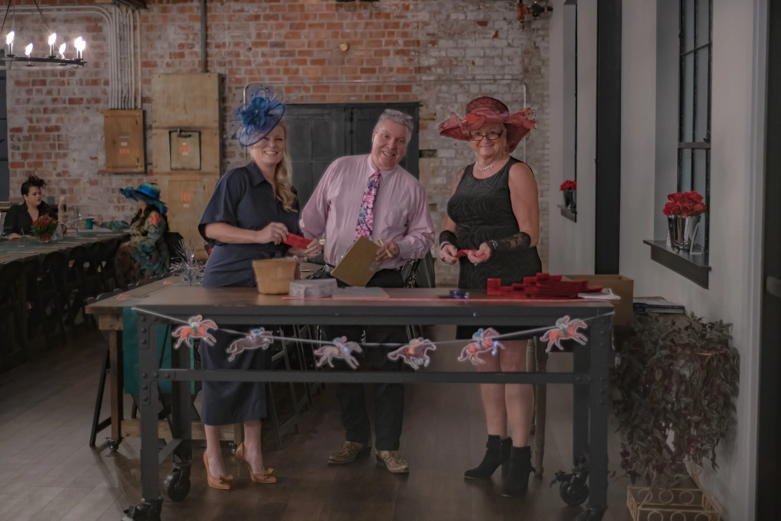 Three people stand behind a cart decorated with horse cutouts; two wear blue and red decorative hats.