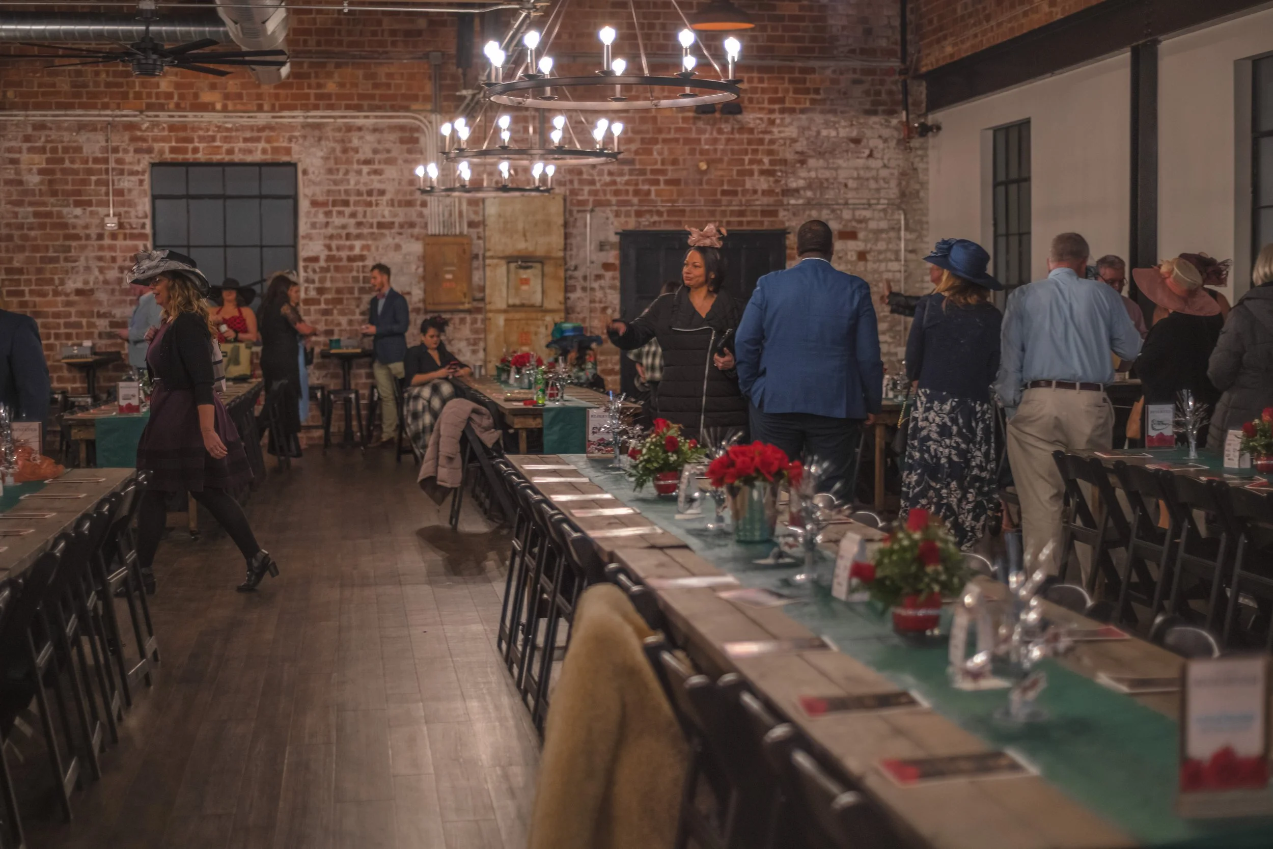 People gather beside a long decorated table, including someone in a blue jacket and others in wide-brimmed hats.
