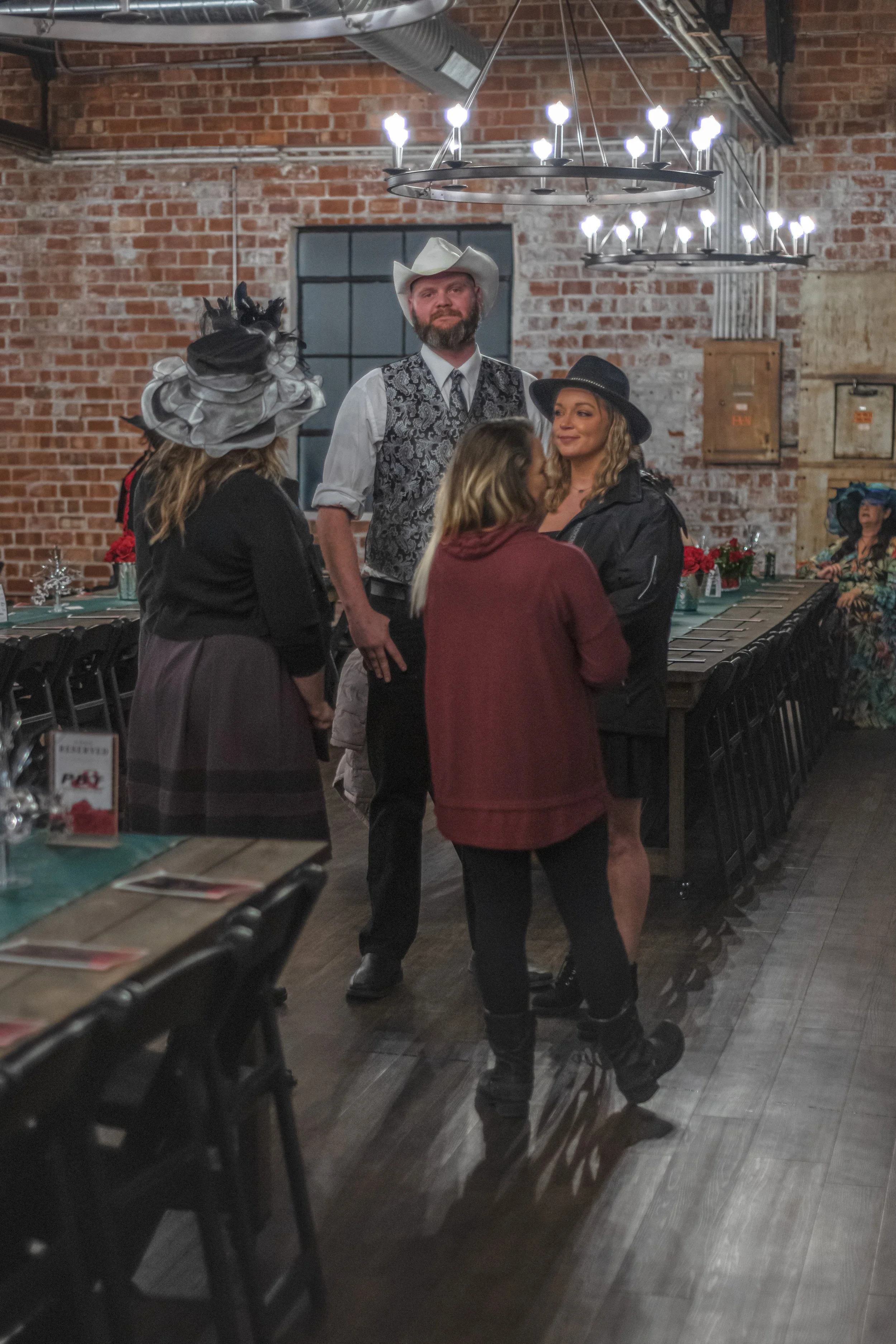 Four people gather beside a banquet table, including someone in a cowboy hat and patterned vest.
