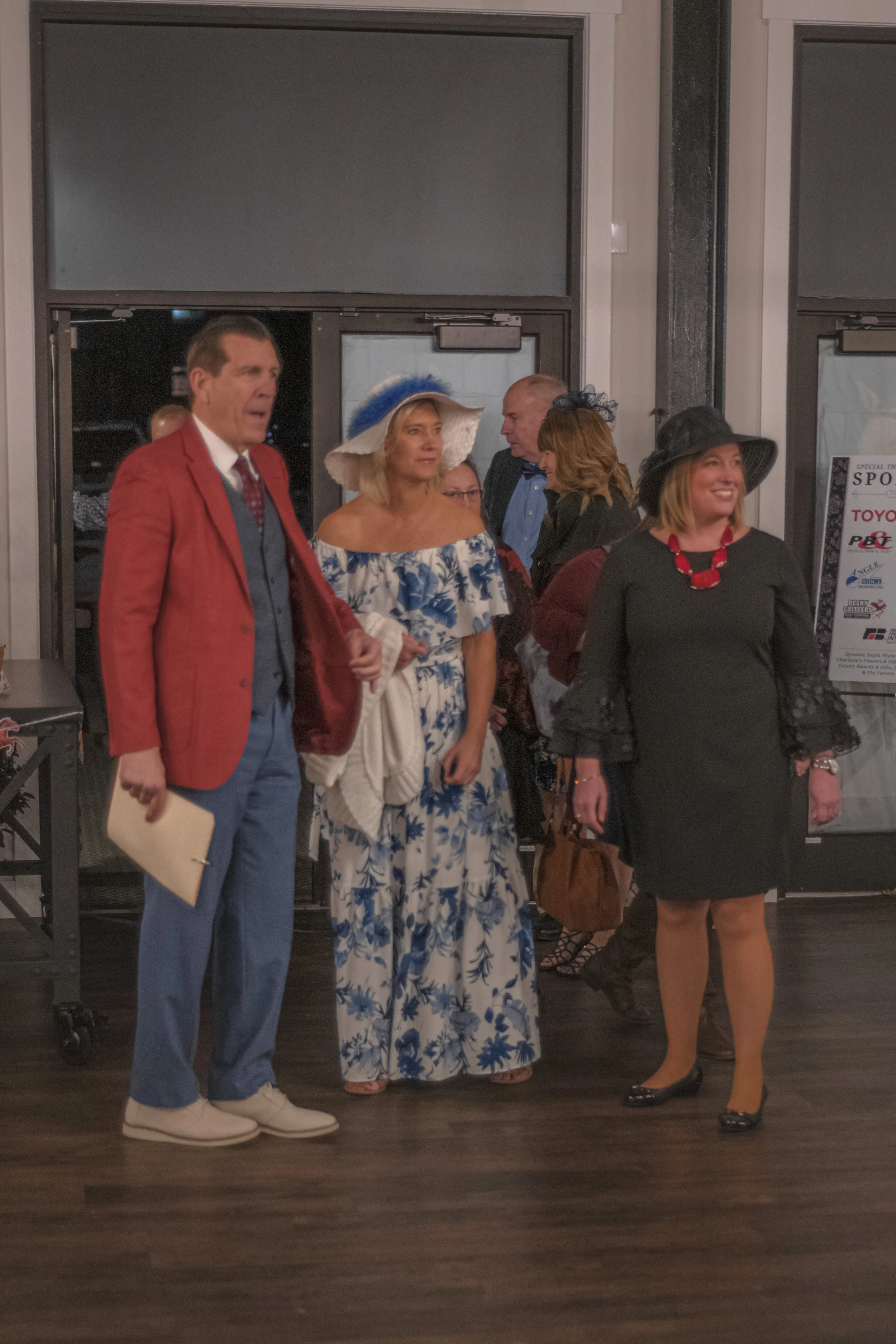 Three people pose by a doorway in a red blazer, a blue-and-white floral dress and a black dress.