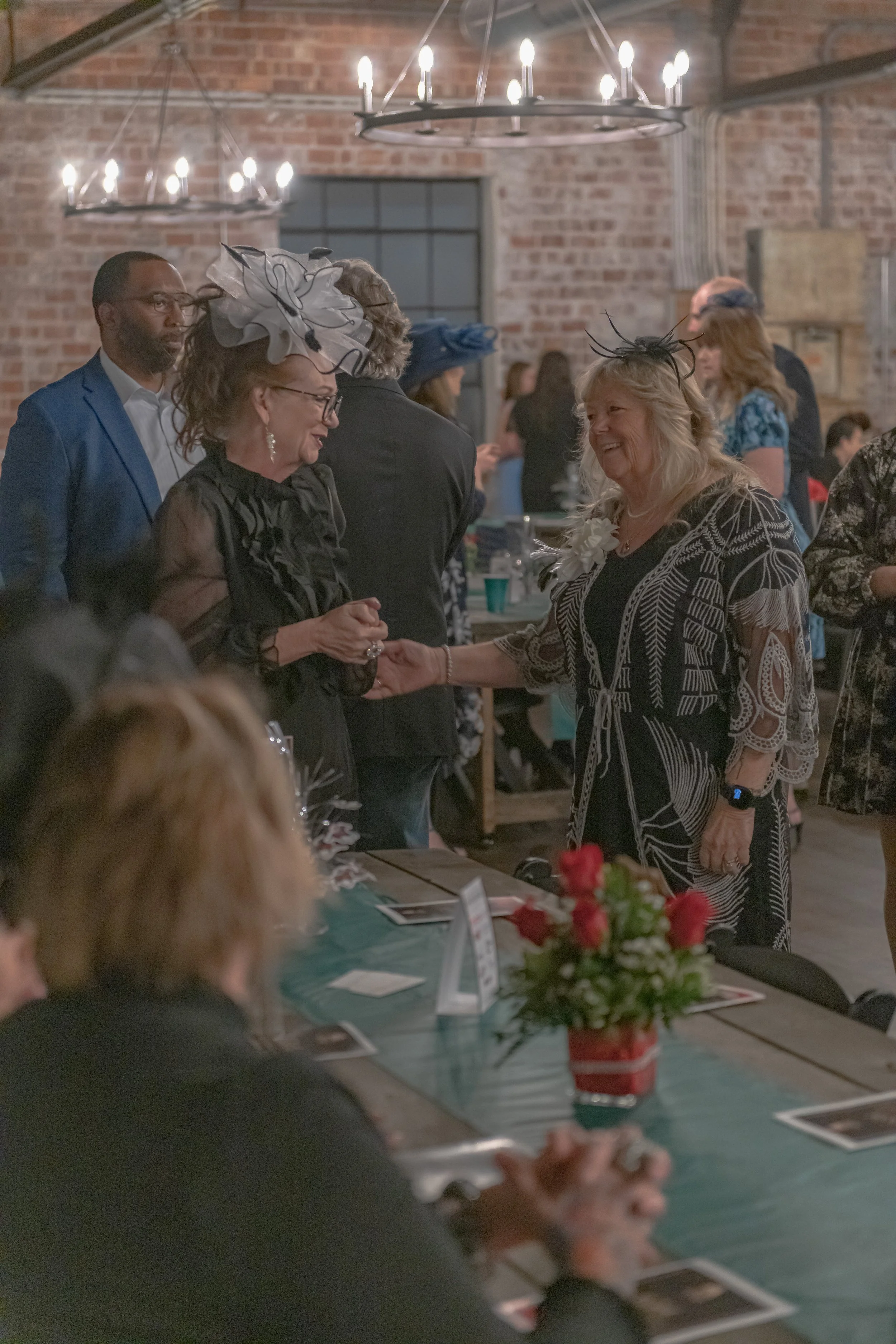 Two people face each other beside a banquet table, one wearing a silver headpiece and the other a white flower corsage.