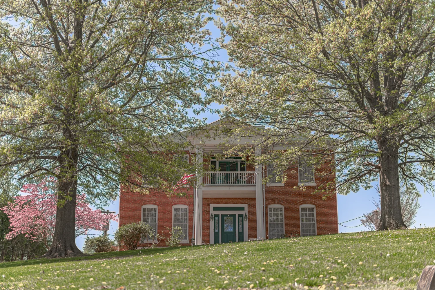 Brick House Framed by Leafy Trees. Visible: brick house, white columns, front entrance.