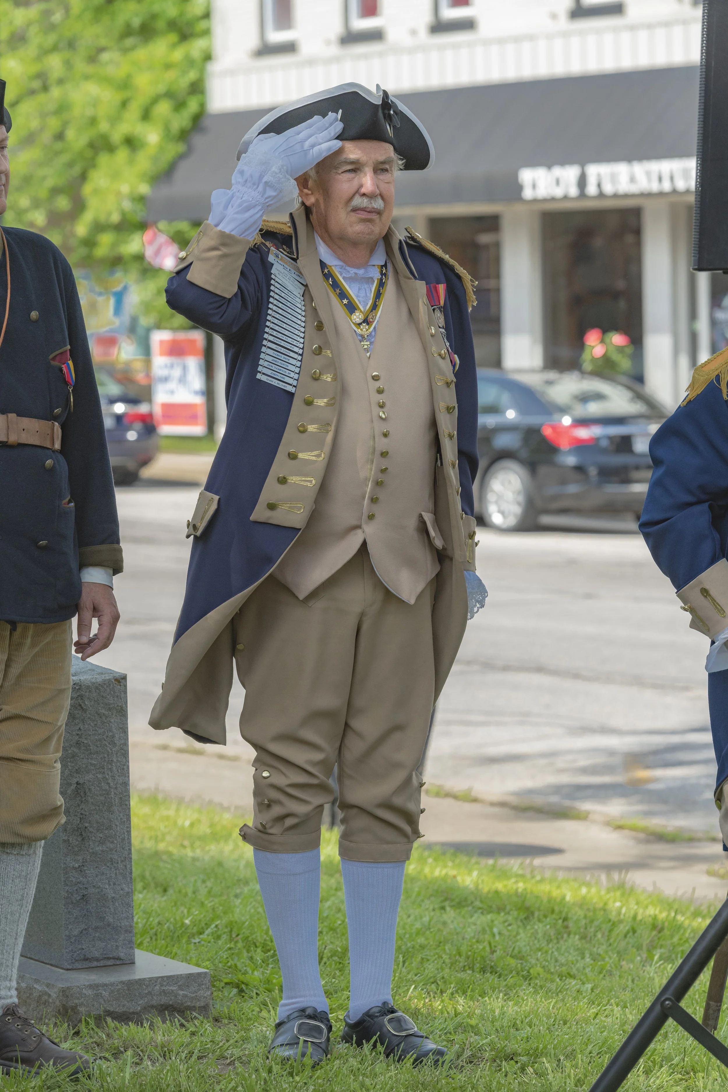 A participant in colonial-style clothing raises a gloved hand in salute at the 2022 Daughters of the American Revolution ceremony.