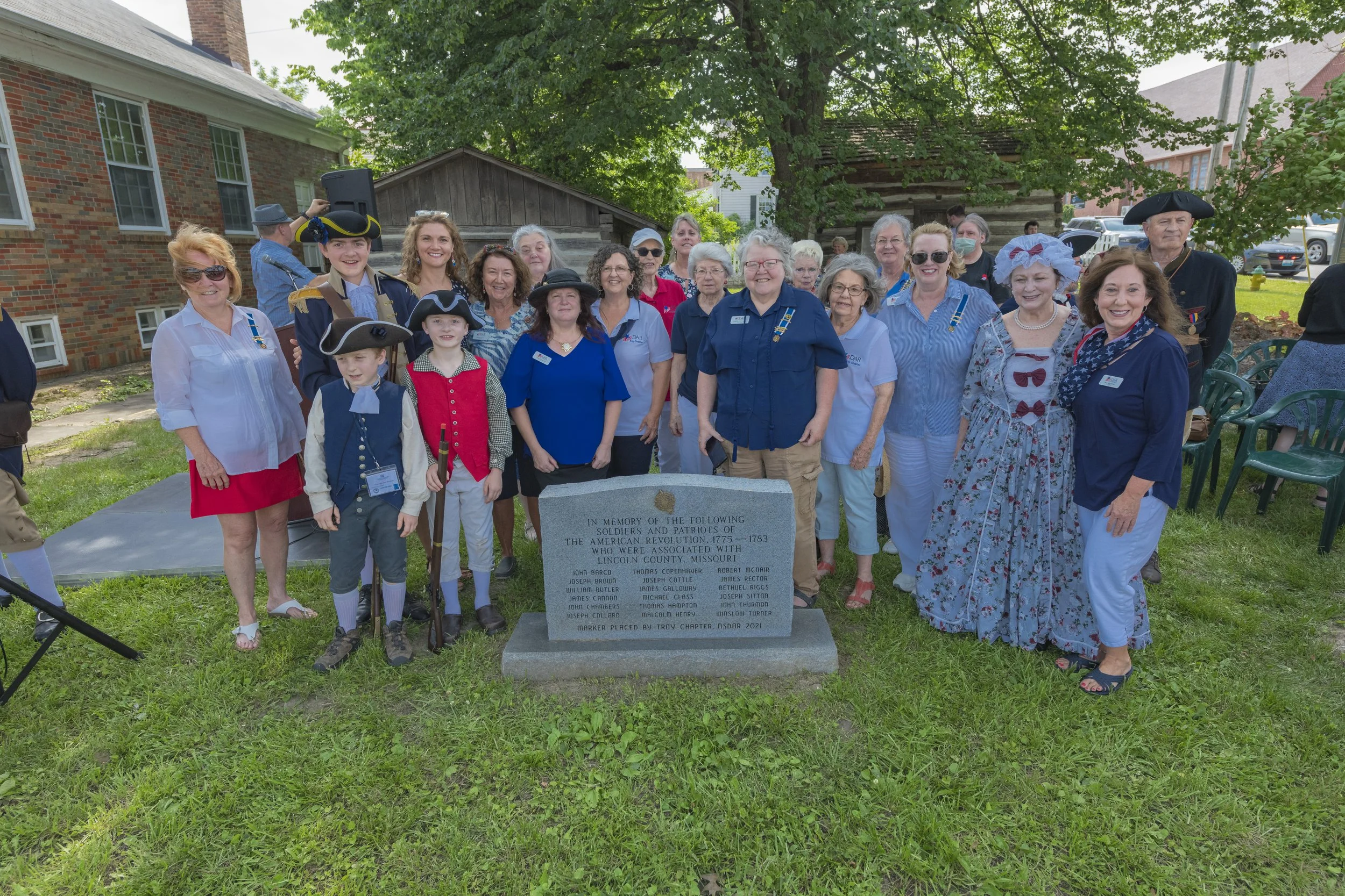 Attendees pose behind a stone marker on the lawn at the 2022 Daughters of the American Revolution ceremony.