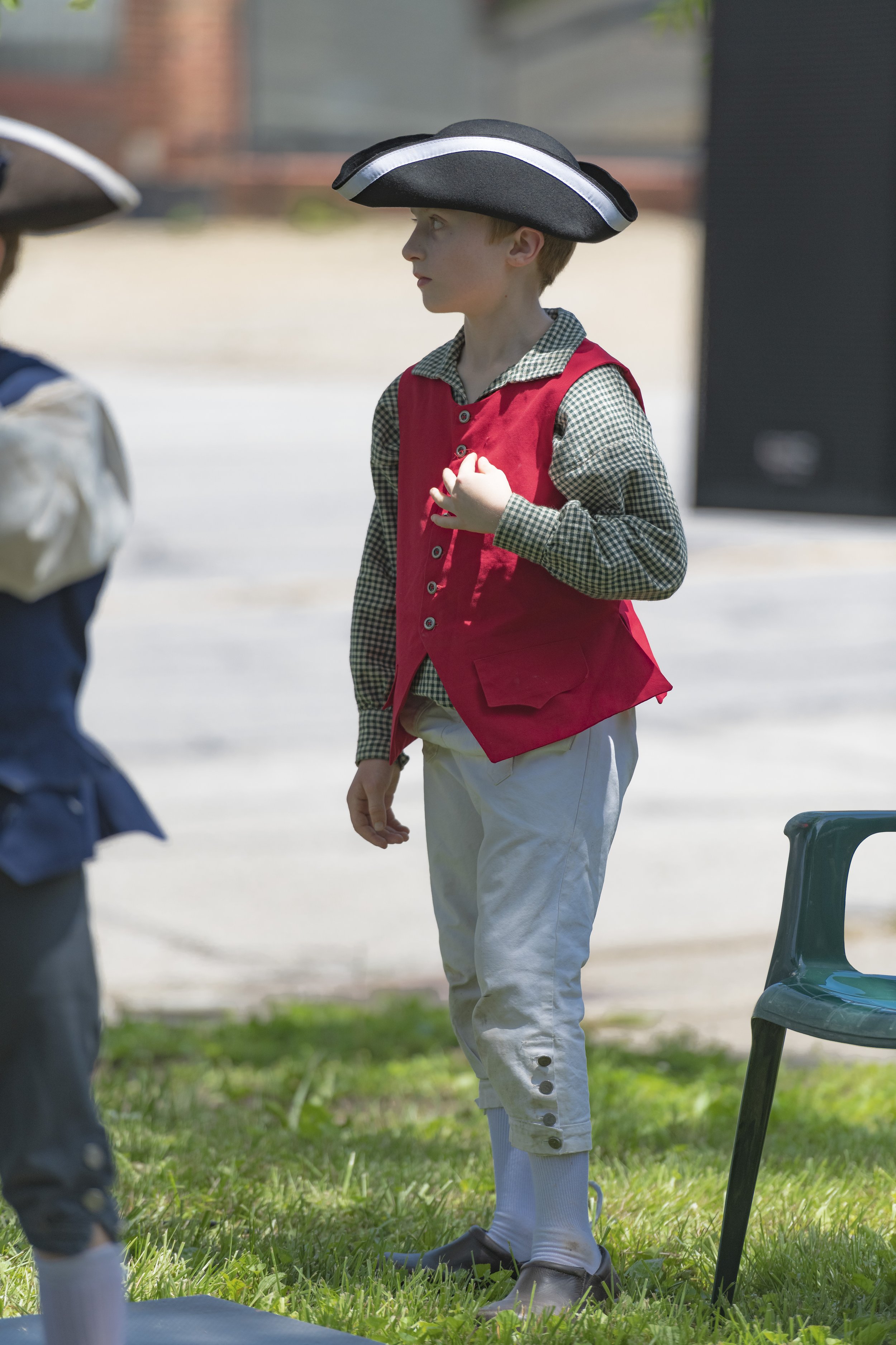 A young participant in a red waistcoat and tricorn hat stands with a hand over the chest at the 2022 Daughters of the American Revolution ceremony.