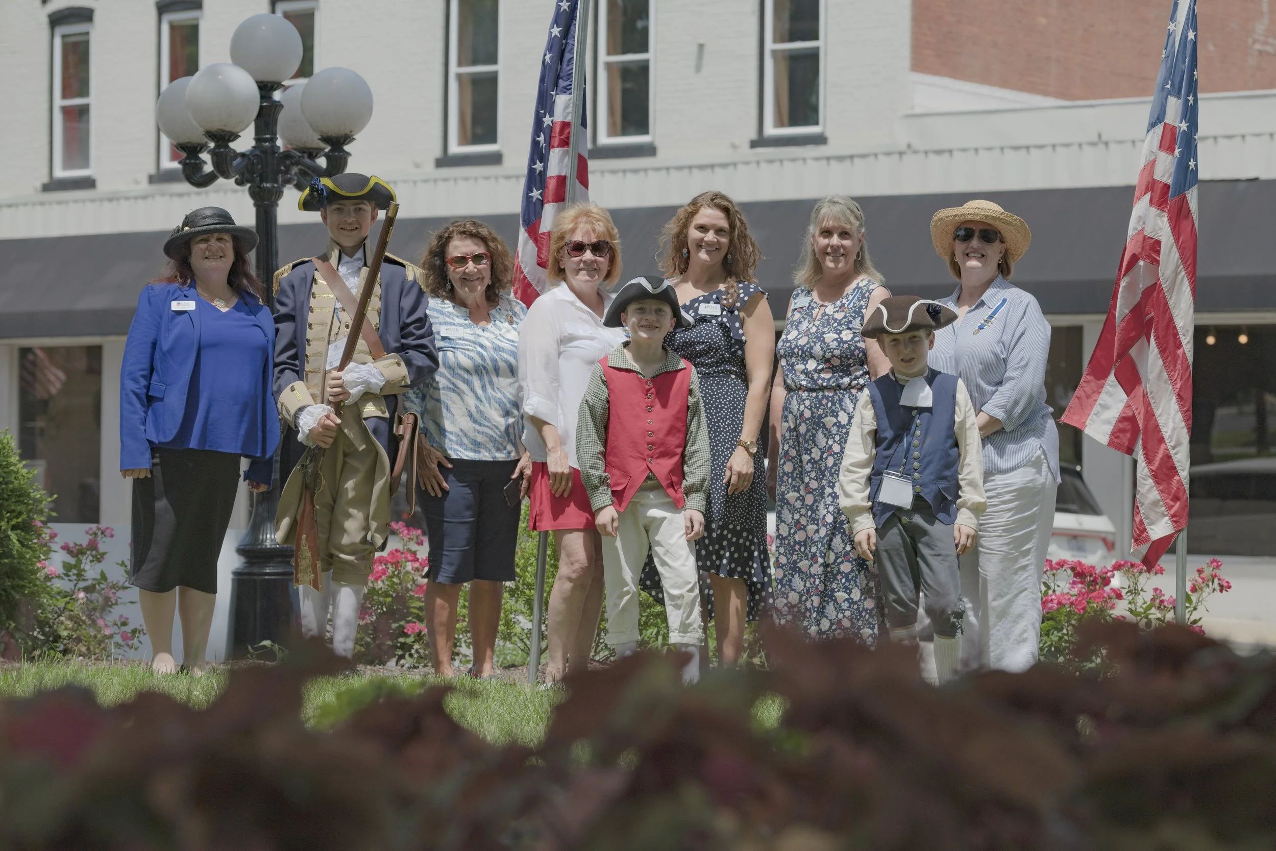 Attendees pose between American flags, with period-dressed participants in the group at the 2022 Daughters of the American Revolution ceremony.