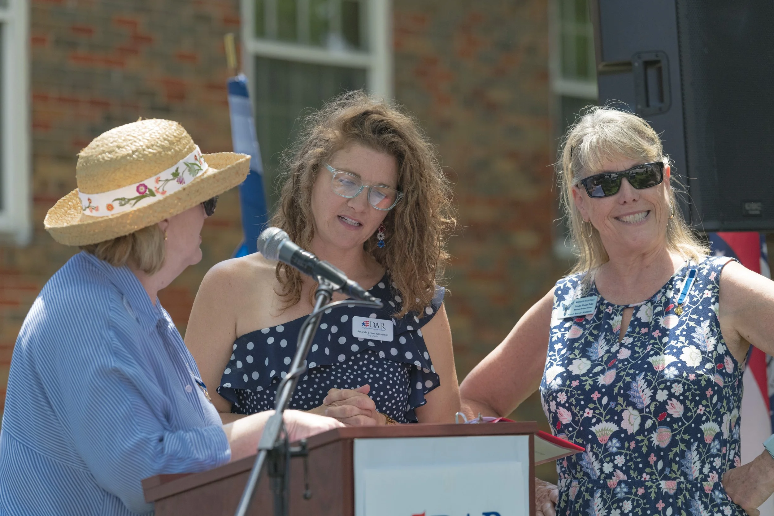 Three participants gather around a document at the lectern at the 2022 Daughters of the American Revolution ceremony.