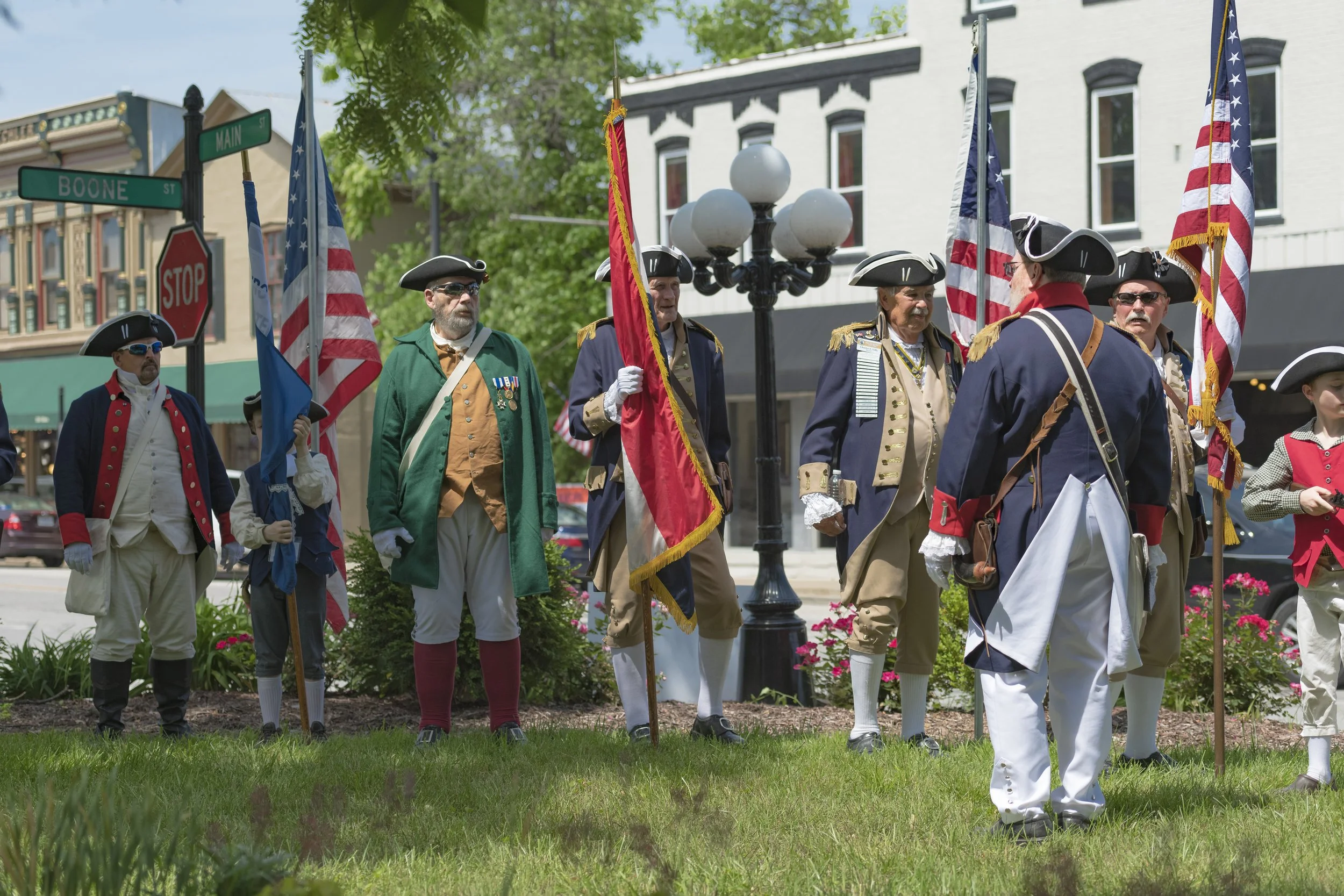 Flag bearers in period clothing stand in formation on the lawn at the 2022 Daughters of the American Revolution ceremony.