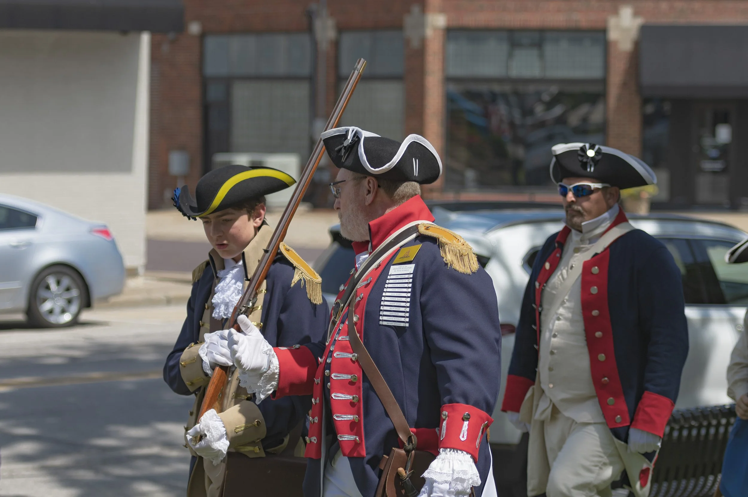 Participants in period uniforms stand together, one holding a long firearm upright at the 2022 Daughters of the American Revolution ceremony.