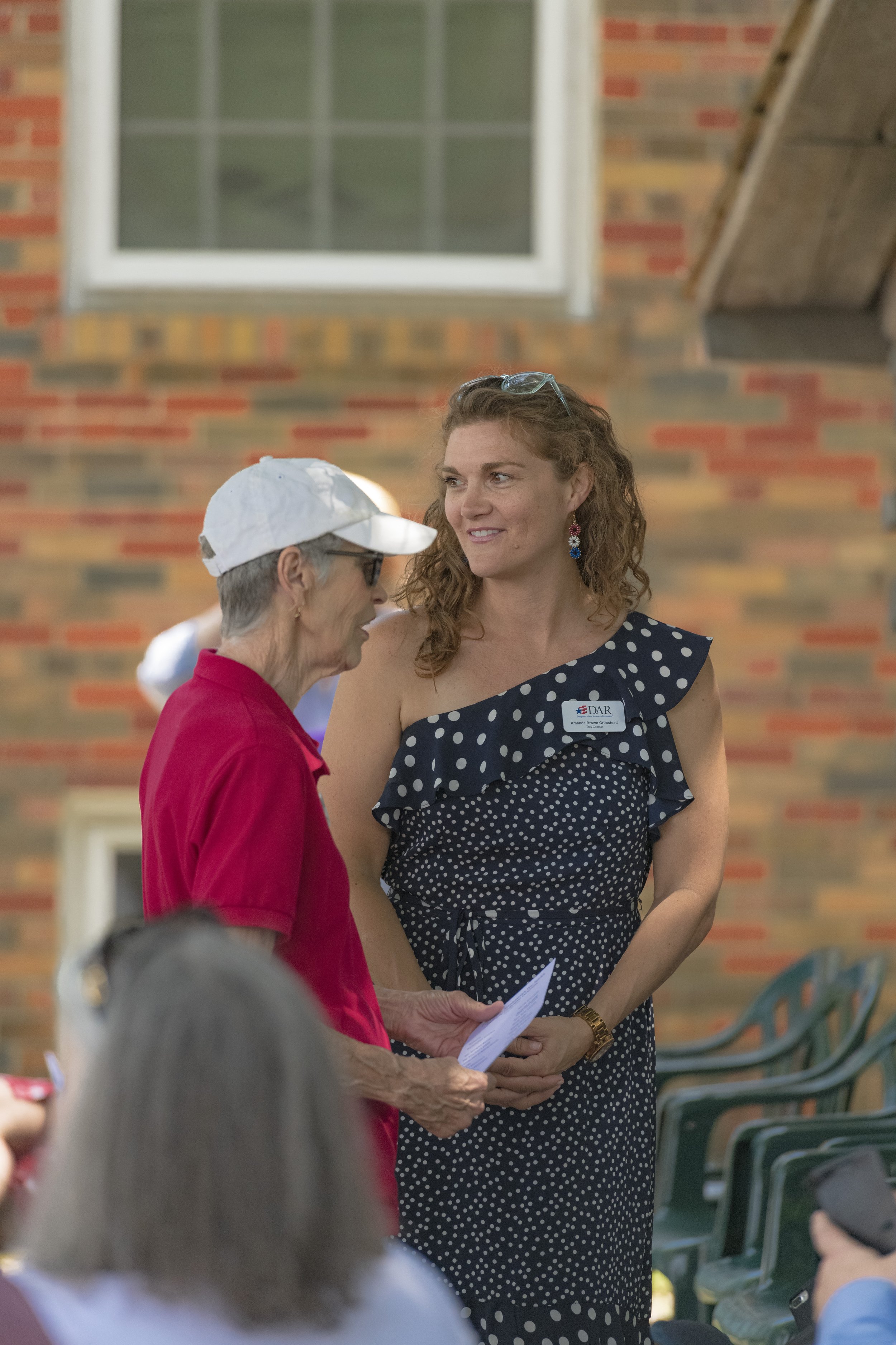 An attendee holding papers talks with another guest beside the brick building at the 2022 Daughters of the American Revolution ceremony.