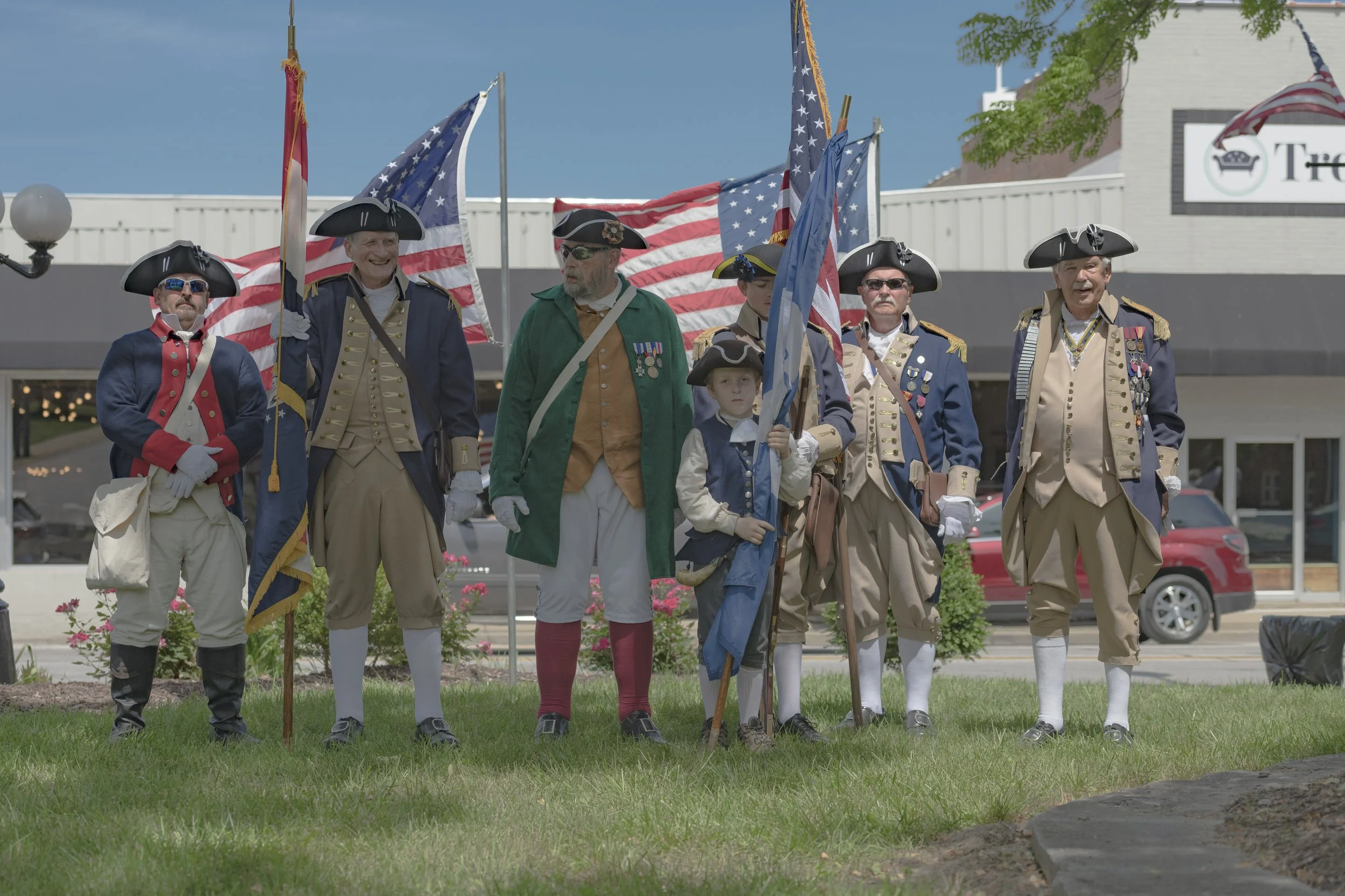 A group in period clothing poses with flags on the lawn at the 2022 Daughters of the American Revolution ceremony.
