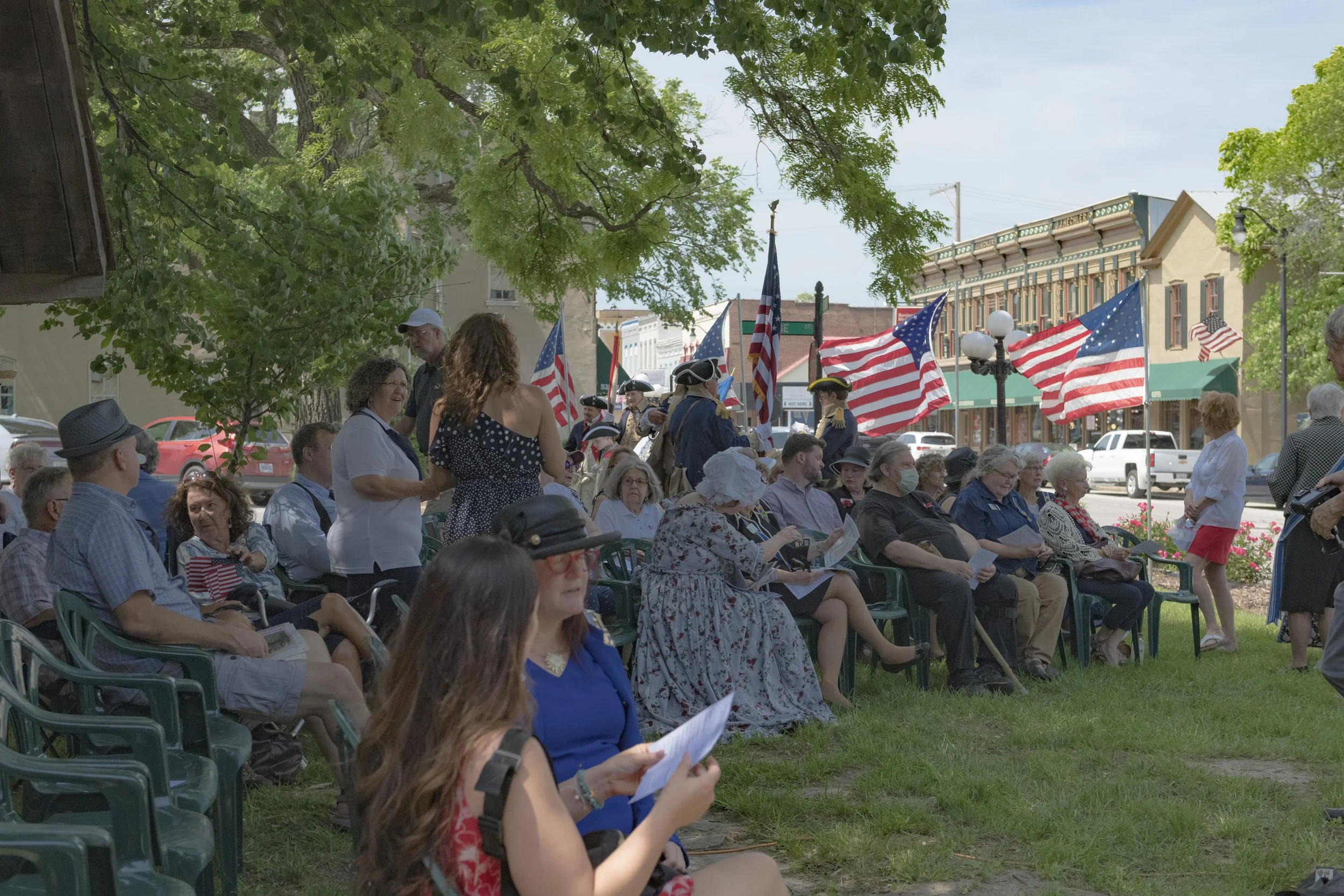 Guests sit in rows beneath the trees with flags behind them at the 2022 Daughters of the American Revolution ceremony.