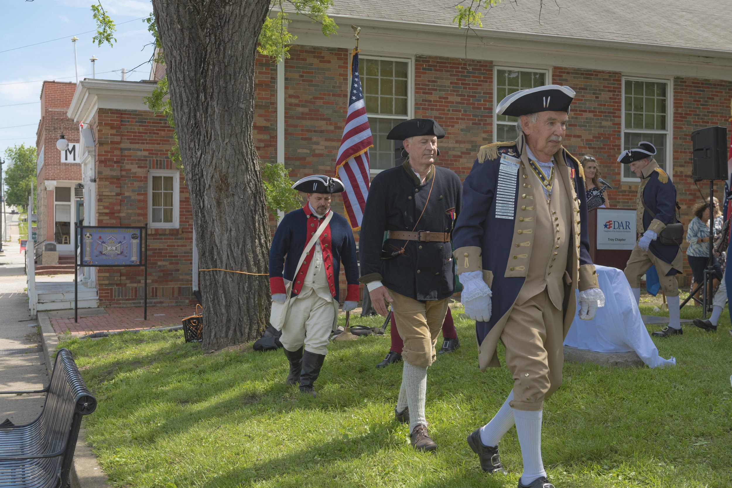 Participants in period uniforms walk across the lawn at the 2022 Daughters of the American Revolution ceremony.