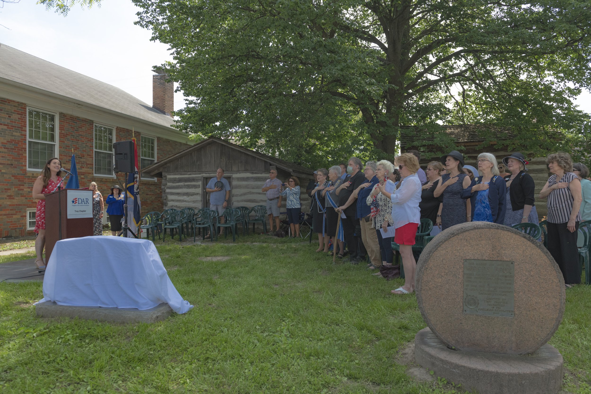 Attendees stand facing the speakers' platform, several with hands over their hearts at the 2022 Daughters of the American Revolution ceremony.
