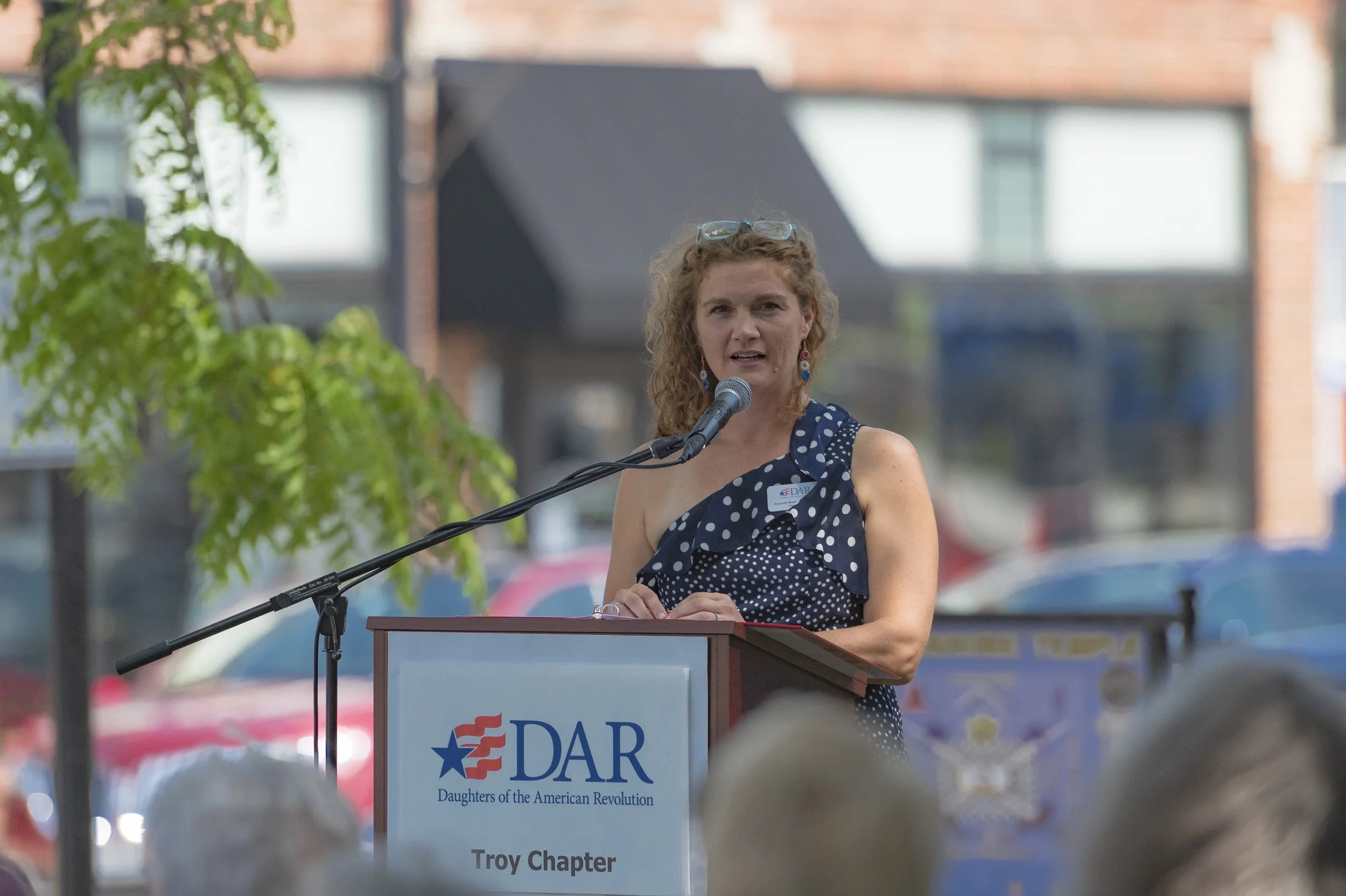A speaker in a navy patterned dress addresses the gathering at the 2022 Daughters of the American Revolution ceremony.