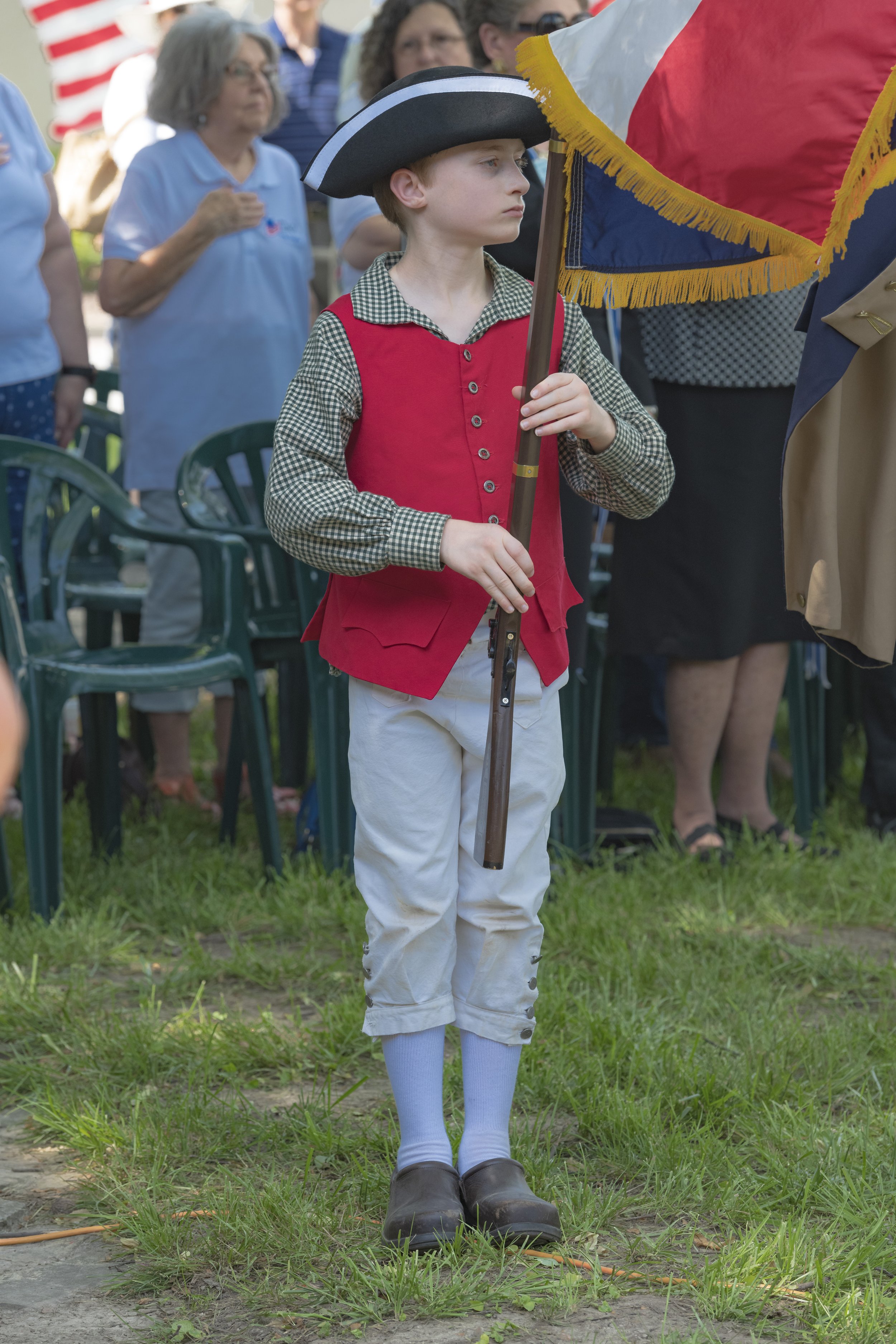A young flag bearer in a tricorn hat holds a flagpole upright at the 2022 Daughters of the American Revolution ceremony.