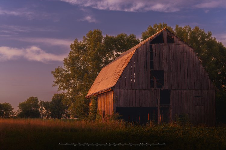 Evening light falls across a weathered barn beneath a purple sky.